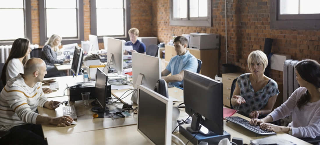 Teamwork 桌布 壁紙 — 一個多元化的專業團隊在一個現代開放式辦公室中協作，辦公室有裸露的磚牆和大窗戶。