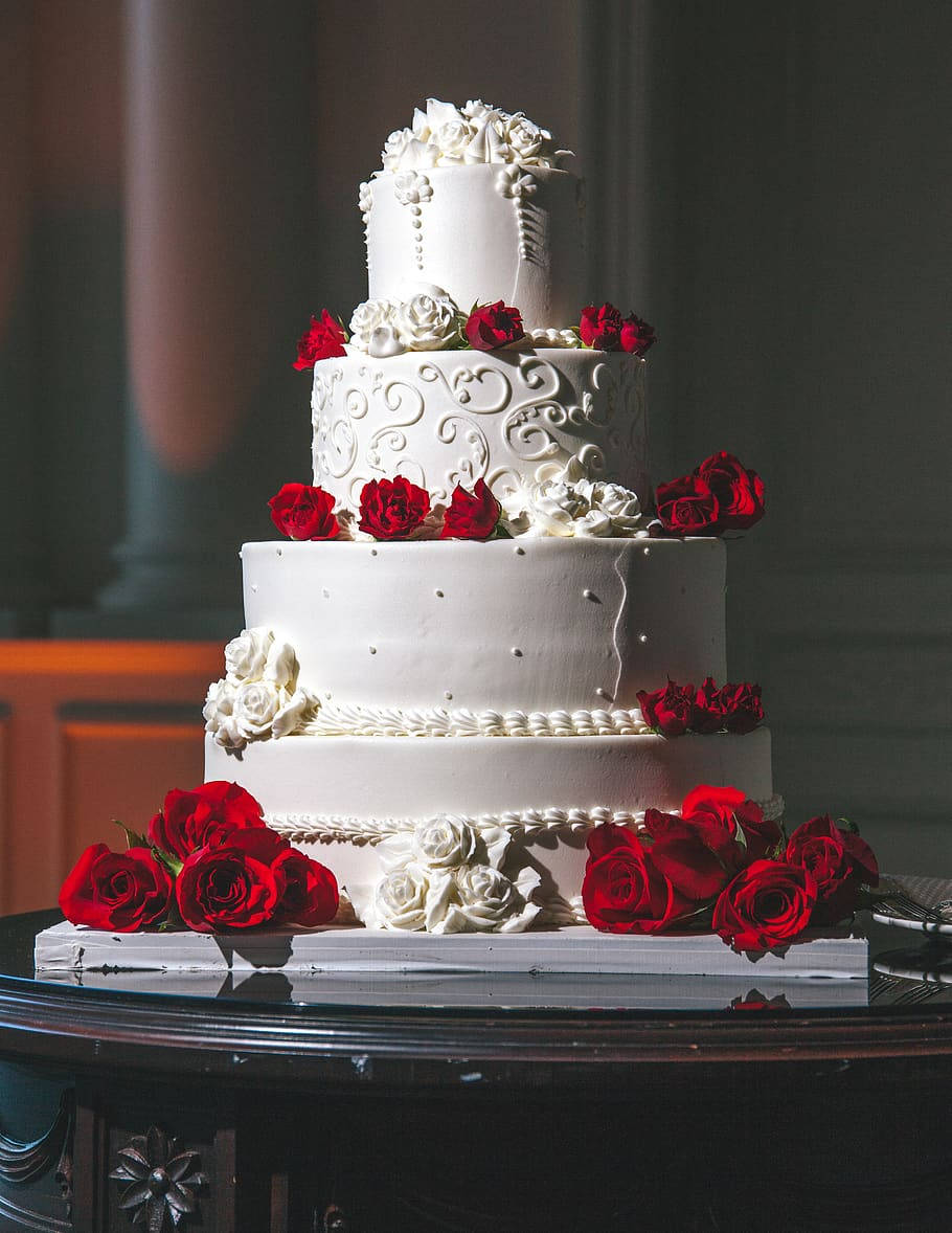 Wedding 桌布 壁紙 — 一個多層白色結婚蛋糕，飾有紅白玫瑰，優雅地擺放在深色木桌上。