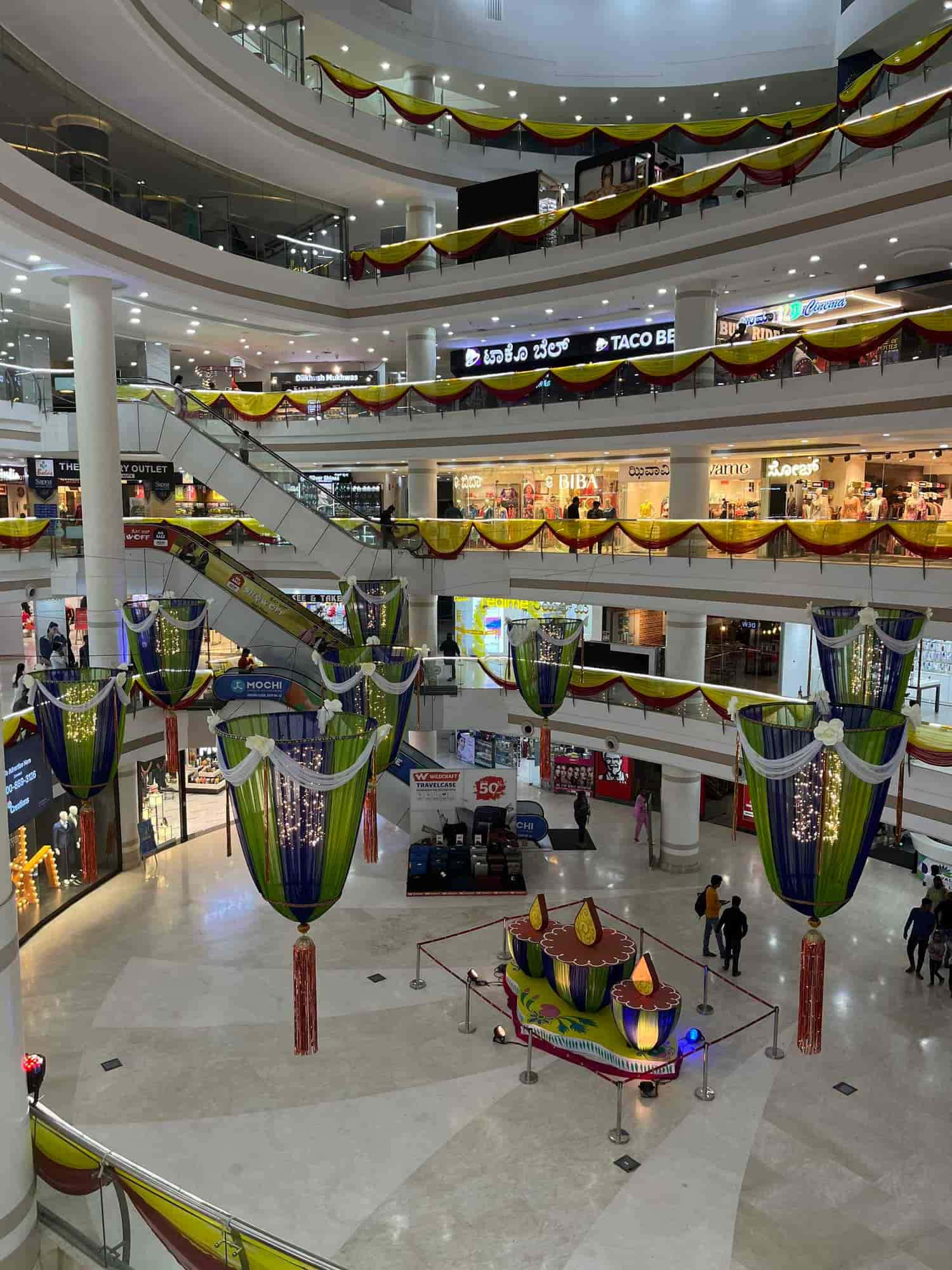 Mall 桌布 壁紙 — 一個多層購物中心，在明亮的頂燈下裝飾著節日黃、紅、綠色的帷幔和懸掛的燈籠。