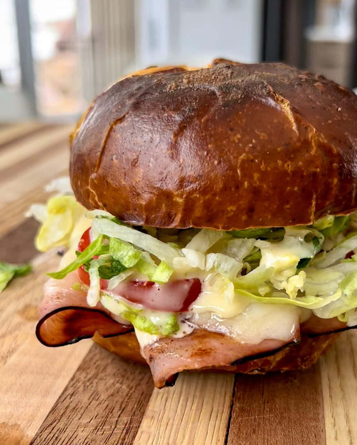 Black Forest Ham 桌布 壁紙 — 一個多汁的椒鹽卷餅包三明治，裡面夾著融化起司、火腿和新鮮生菜，放在木板上特寫。