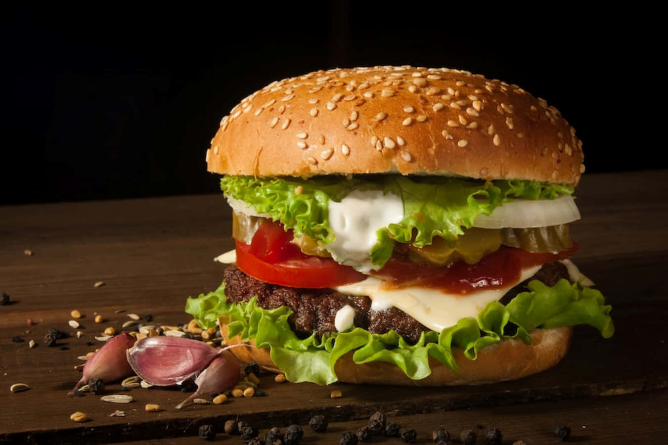 fast food 桌布 壁紙 — 一個多汁的漢堡，上面有融化的起司、番茄、生菜和酸黃瓜，放在木板上，周圍有蒜頭和胡椒粒。