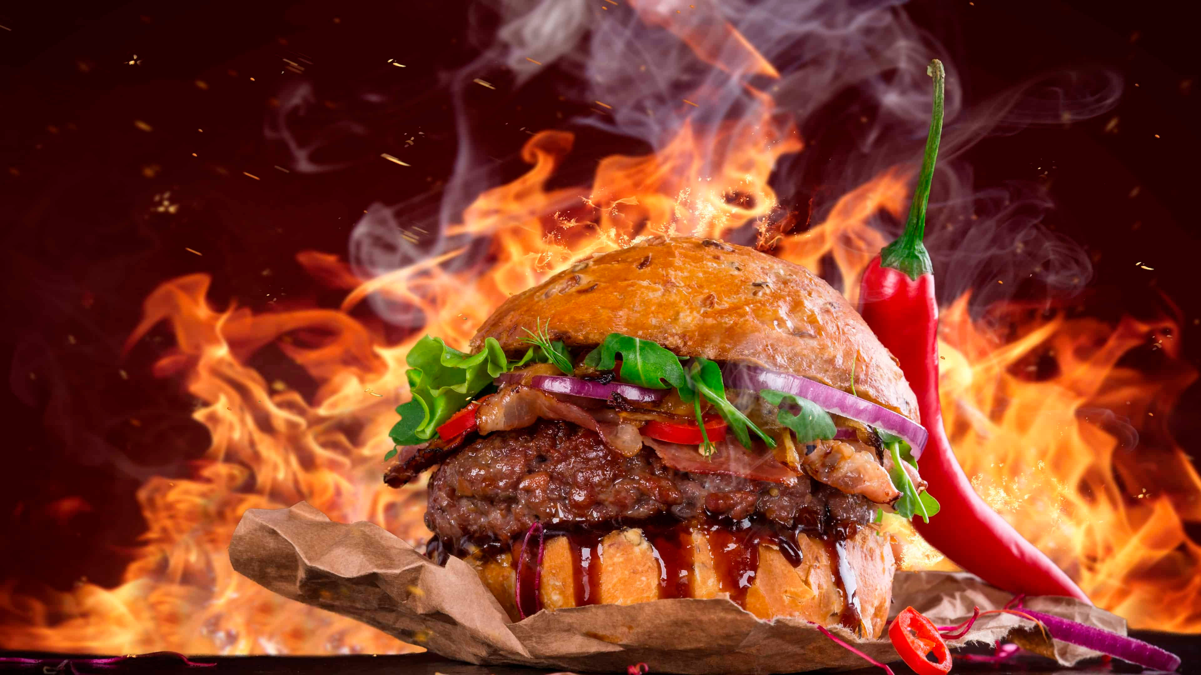 Burger 桌布 壁紙 — 一個多汁的漢堡，配上培根、生菜和醬汁，在紅辣椒旁邊的熊熊烈火中燜燒。