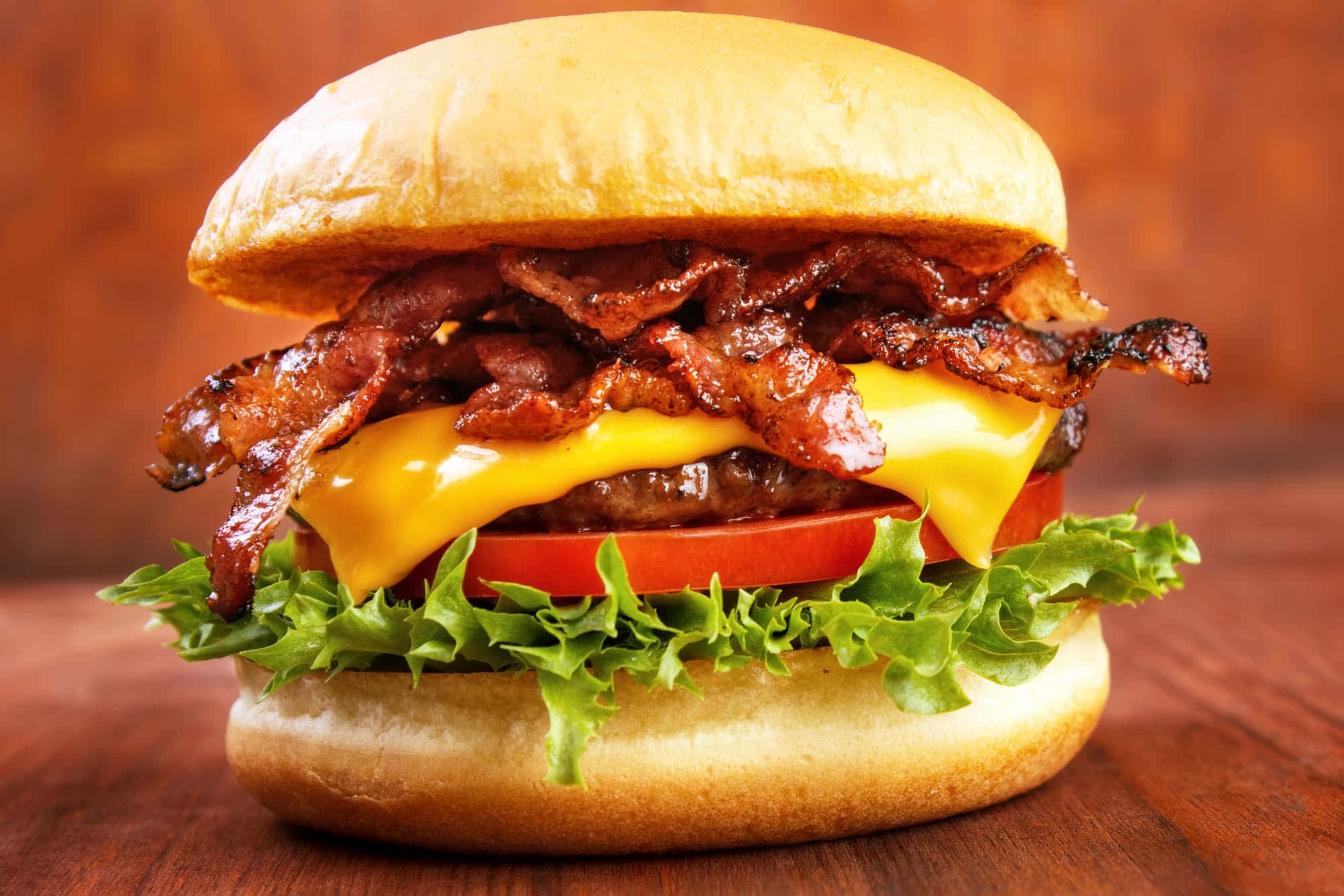 bacon 桌布 壁紙 — 一個多汁的漢堡，配上脆培根、融化起司、番茄和生菜，放在木質表面上。