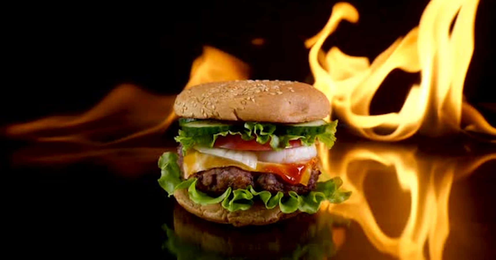 fast food 桌布 壁紙 — 一個多汁的漢堡，配上融化的起司和新鮮蔬菜，在反射表面上傲然面對咆哮的火焰。