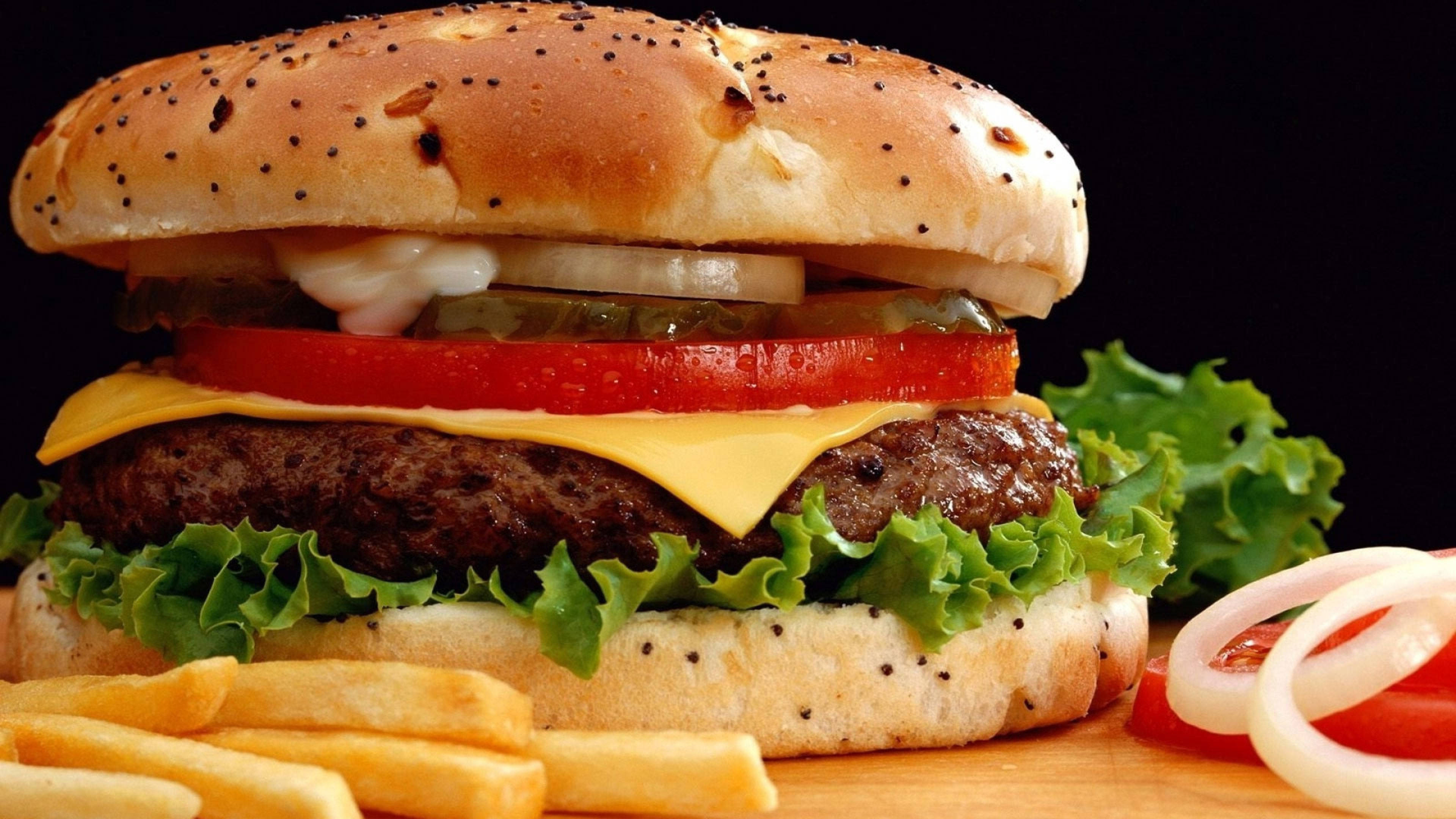 Food Photography 桌布 壁紙 — 一個多汁的漢堡，配上融化起司、番茄和生菜，放在罌粟籽麵包上，旁邊有脆薯條和洋蔥圈。
