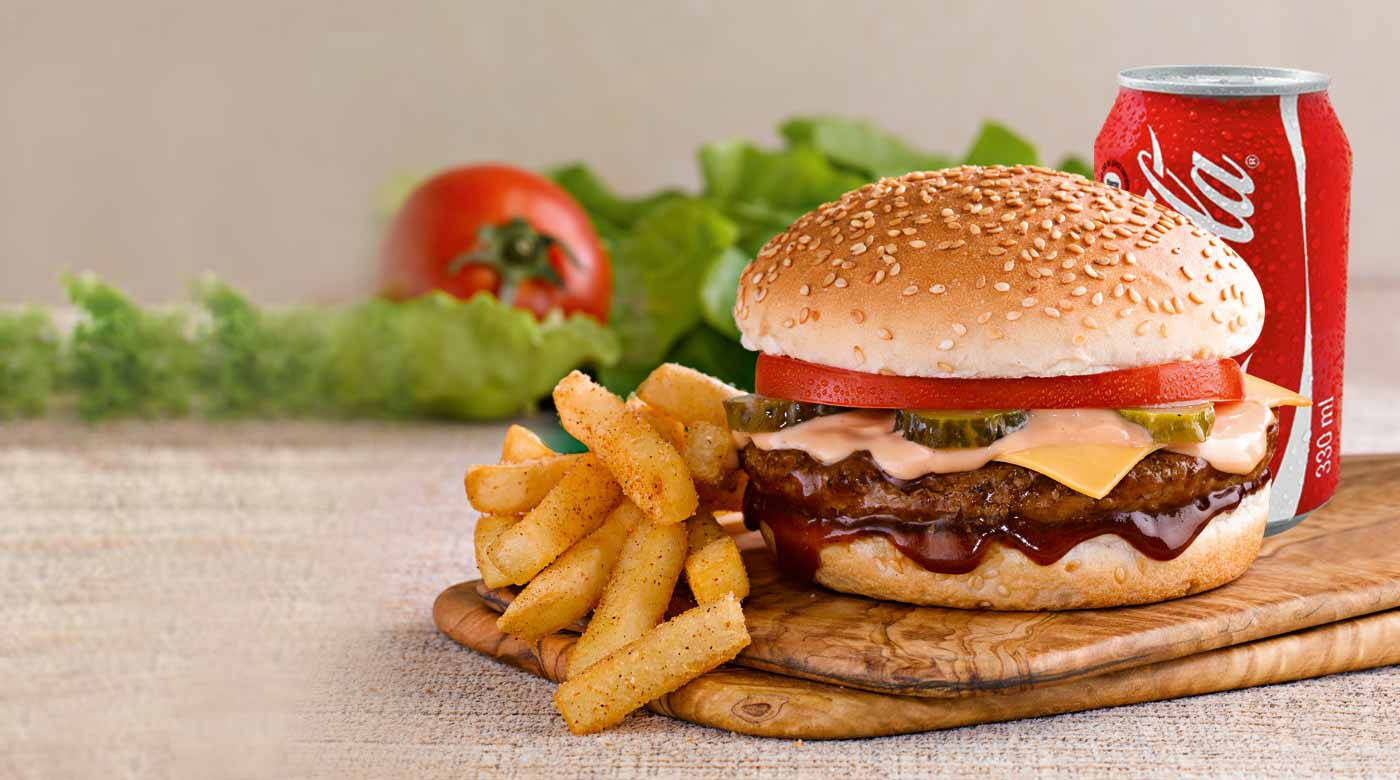 Burger 桌布 壁紙 — 一個多汁的漢堡，配上起司、酸黃瓜和醬汁，旁邊有酥脆薯條和一罐可口可樂，放在木板上。