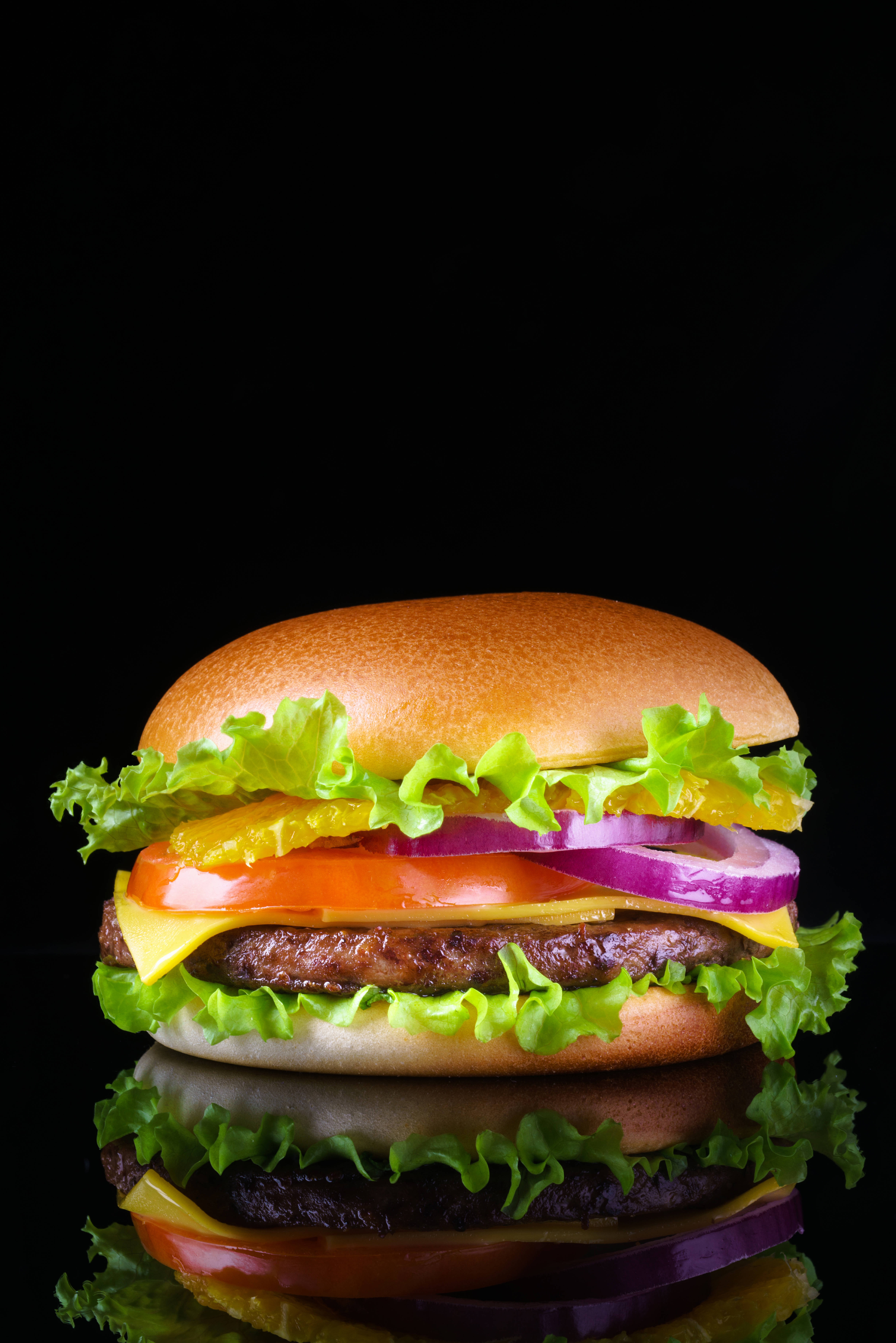 Food Photography 桌布 壁紙 — 一個多汁的漢堡，配有生菜、番茄、起司和洋蔥，放在黑色反光表面上。