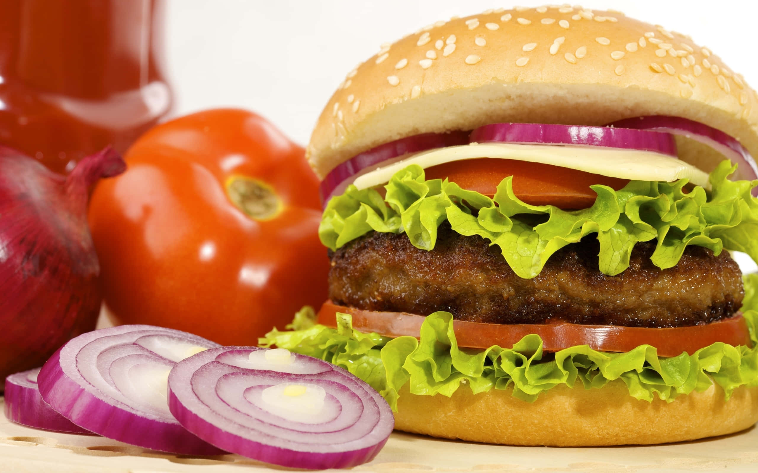 hamburger 桌布 壁紙 — 一個多汁的漢堡，配有生菜、番茄和洋蔥，旁邊是新鮮的紅甜椒和切片紅洋蔥，放在木質表面上。