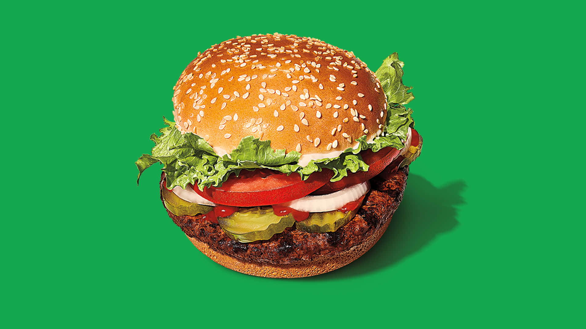 Burger King 桌布 壁紙 — 一個多汁的漢堡，配有芝麻麵包、番茄、生菜、洋蔥和醃黃瓜，在充滿活力的綠色背景前。