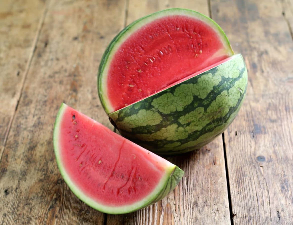 Watermelon 桌布 壁紙 — 一個多汁的西瓜在質樸的木桌上切開，露出鮮紅的果肉和綠色的外皮。