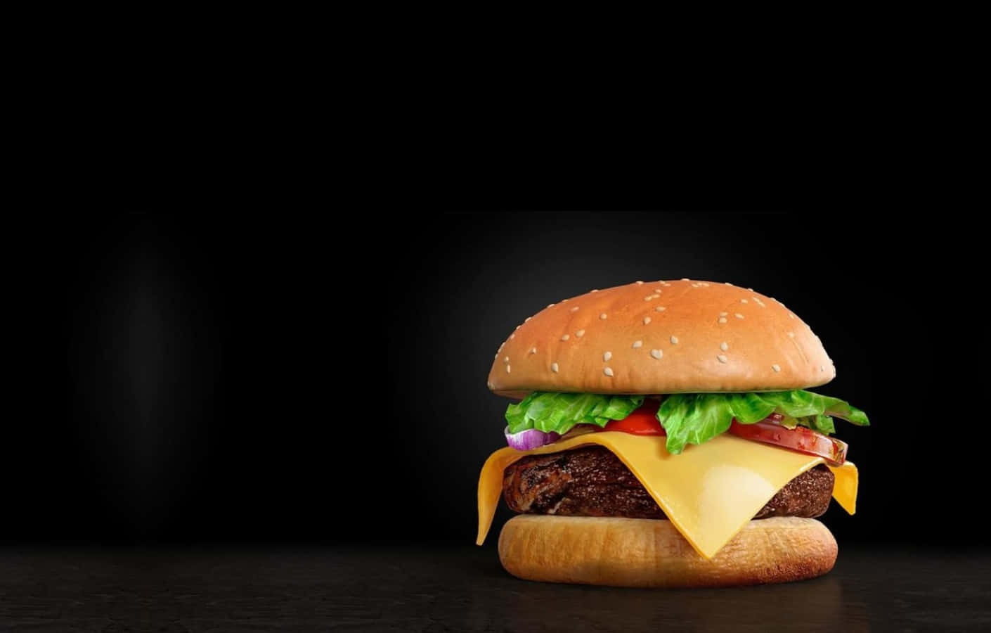 fast food 桌布 壁紙 — 一個多汁的起司漢堡，搭配芝麻麵包、生菜、番茄和融化起司，置於純黑色背景中央。