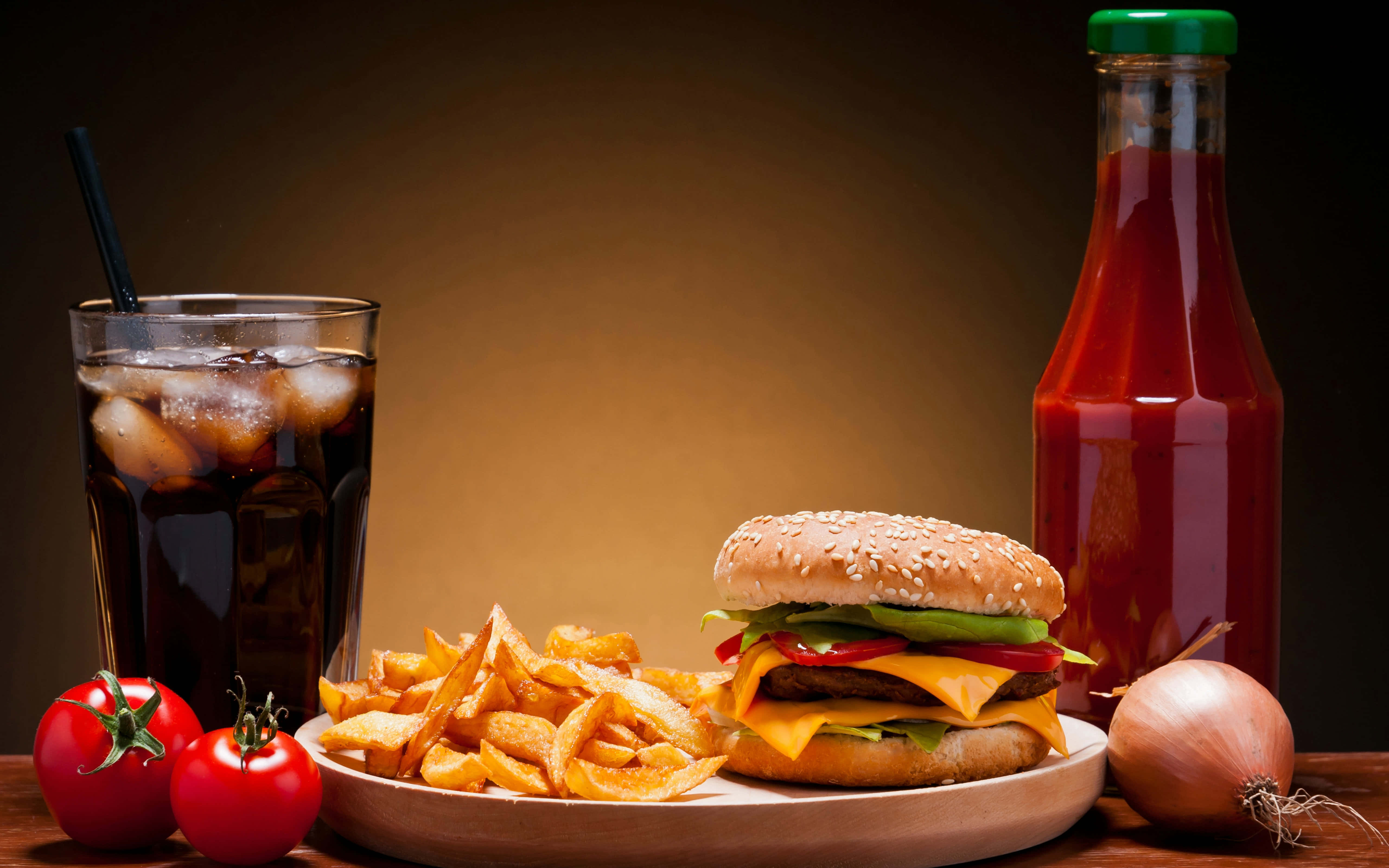 Food And Beverage 桌布 壁紙 — 一個多汁的起司漢堡配薯條和一杯可樂，旁邊有番茄醬瓶和新鮮番茄在木桌上。