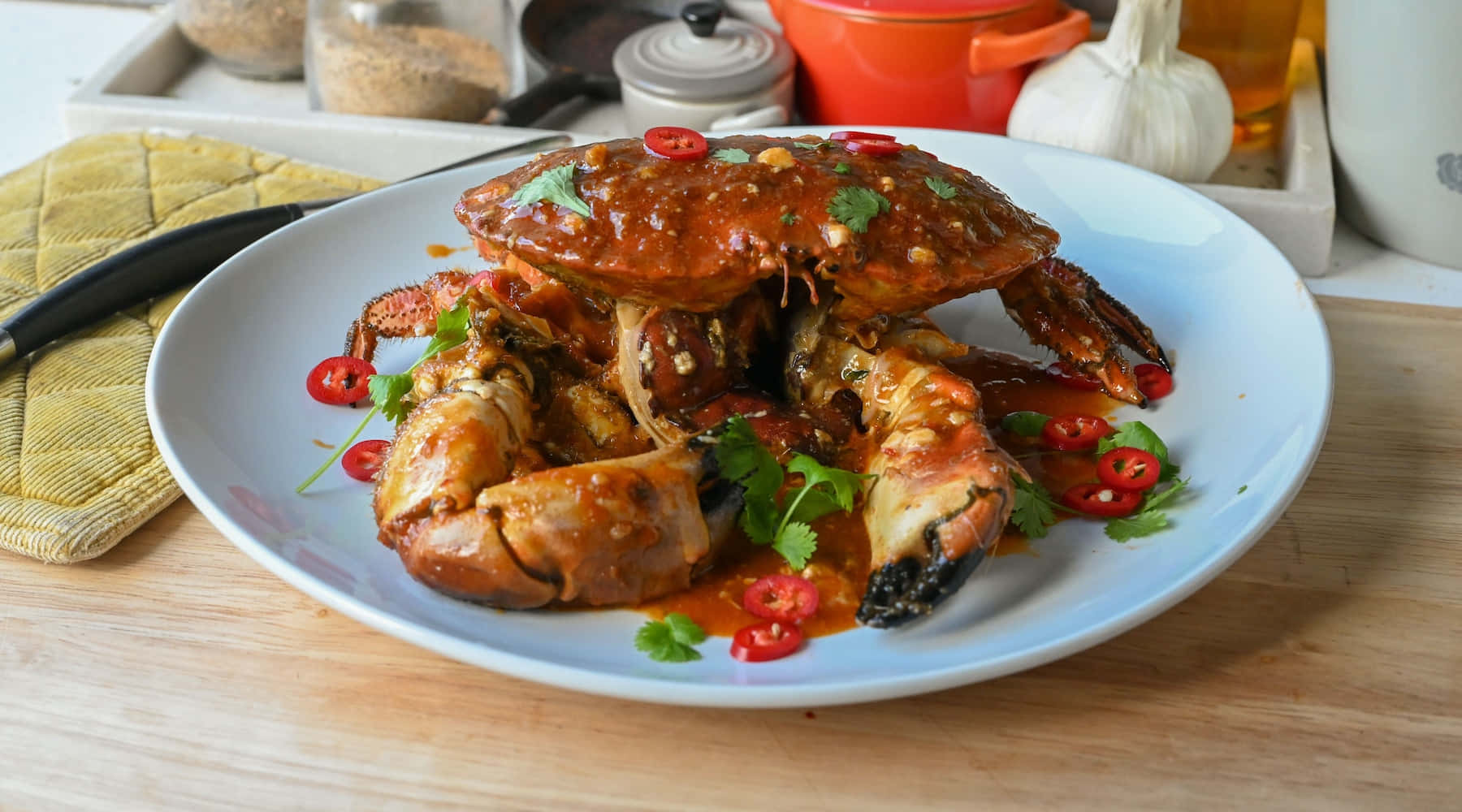 Spicy 桌布 壁紙 — 一個多汁的辣椒蟹菜餚，在木桌上的白色碟子上閃爍著醬汁和新鮮香菜。