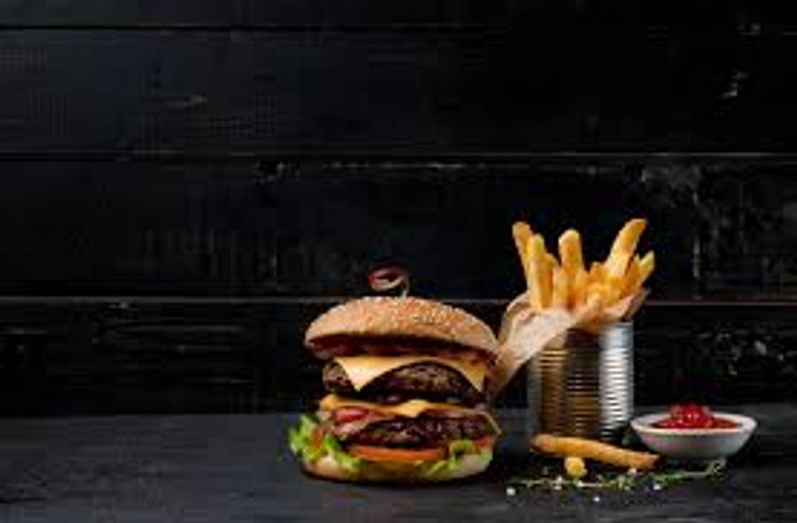 Burger King 桌布 壁紙 — 一個多汁的雙層漢堡，配上融化的起司和新鮮生菜，旁邊是放在深色木桌上罐子裡的金黃酥脆薯條。