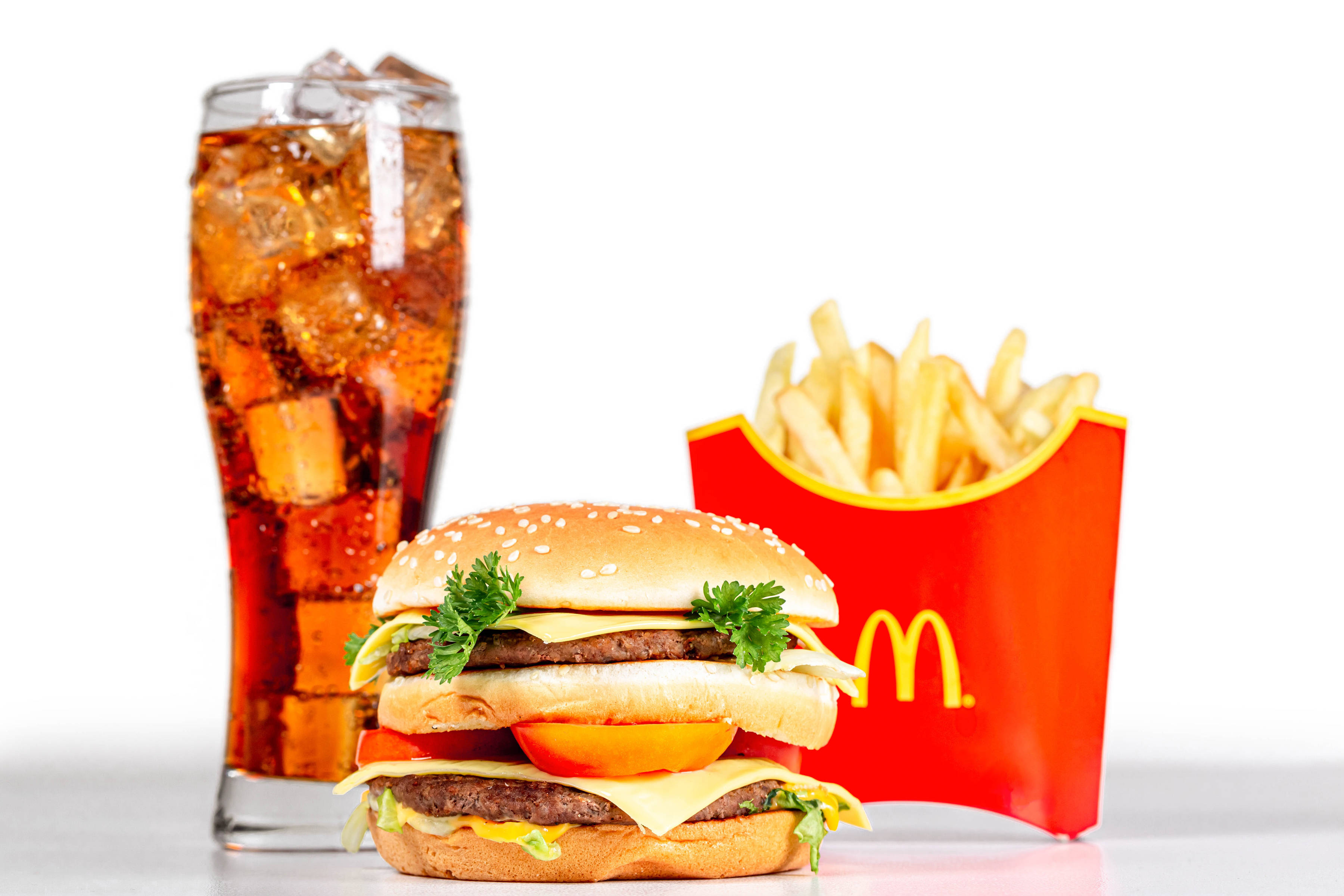 Mcdonalds 桌布 壁紙 — 一個多汁的雙層漢堡配上新鮮配料，旁邊放著一杯冰可樂和一個紅色薯條盒，背景是潔淨的白色。