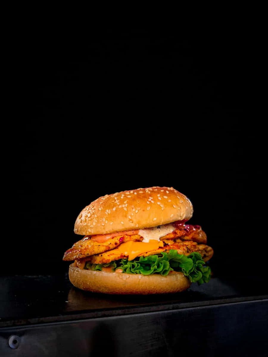fast food 桌布 壁紙 — 一個多汁的雞肉漢堡，配上融化的起司和新鮮的生菜，放在芝麻麵包上，背景是純黑色。