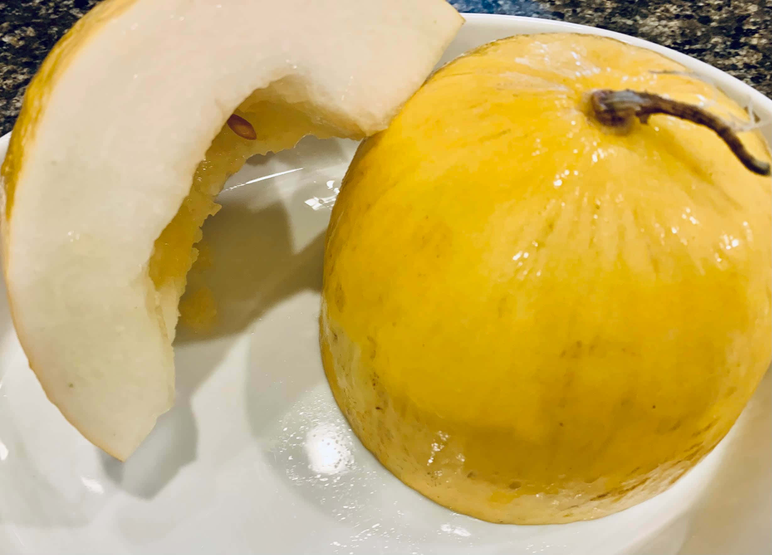 Food Photography 桌布 壁紙 — 一個多汁的黃色蜜瓜，切去一片，放在白色盤子上，背景是深色有斑點的檯面。