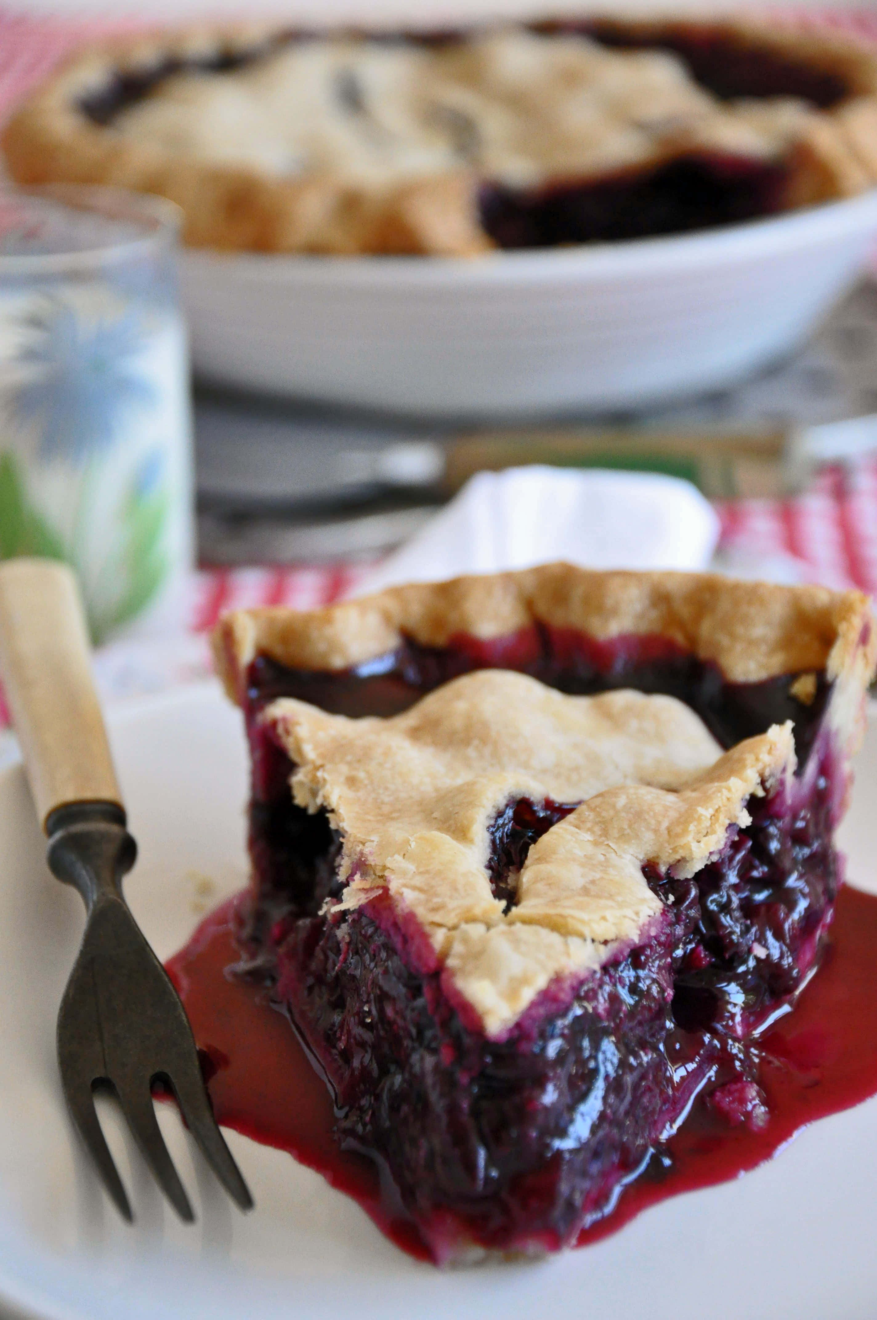 Blueberry Pie 桌布 壁紙 — 一個多汁藍莓派的近距離特寫，金黃色外皮搭配糖漿內餡，放在白色盤子上。