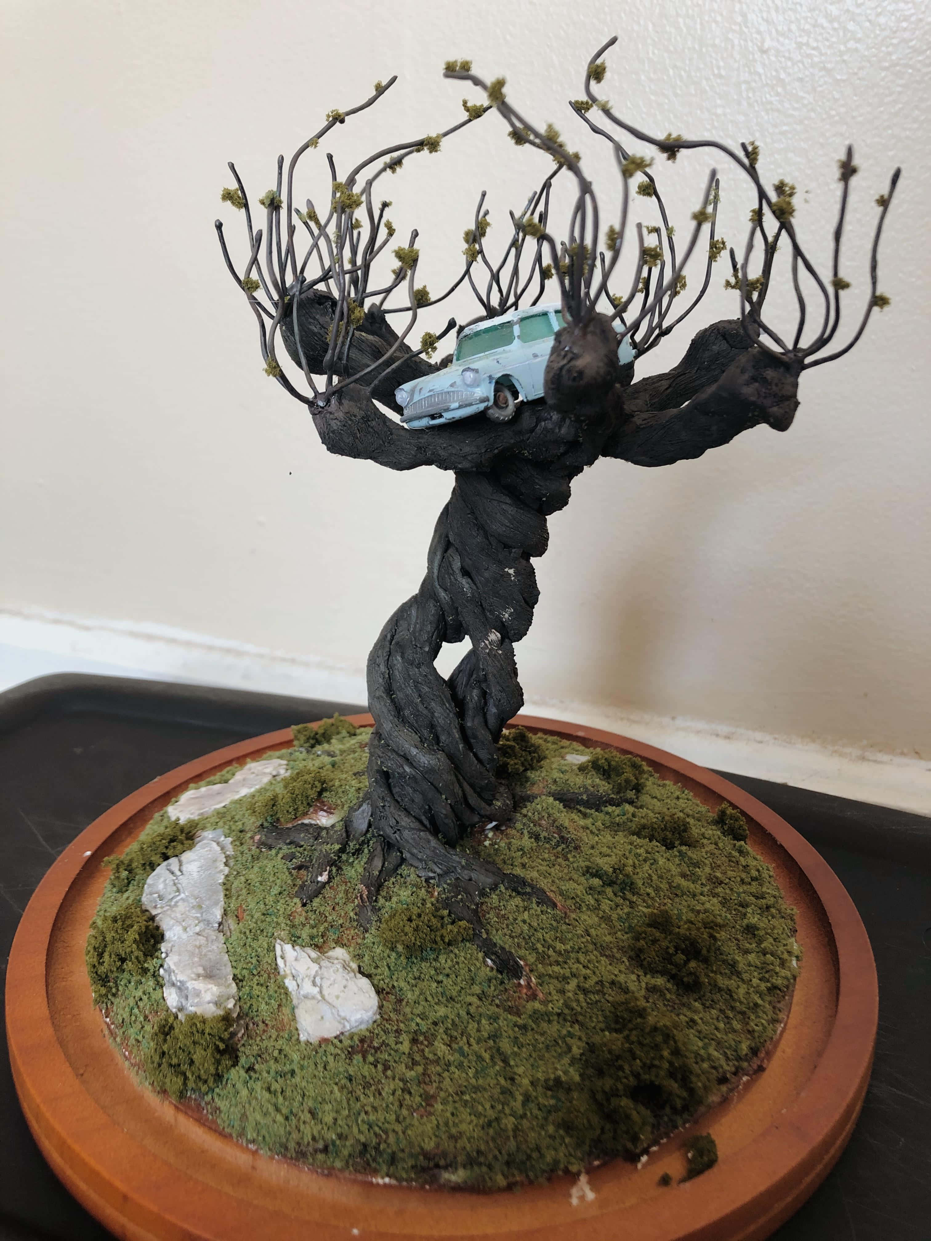 The Whomping Willow 桌布 壁紙 — 一個多節的樹木雕塑，淺藍色復古汽車棲息在光禿禿的樹枝之間，底座是長滿苔蘚的木頭。