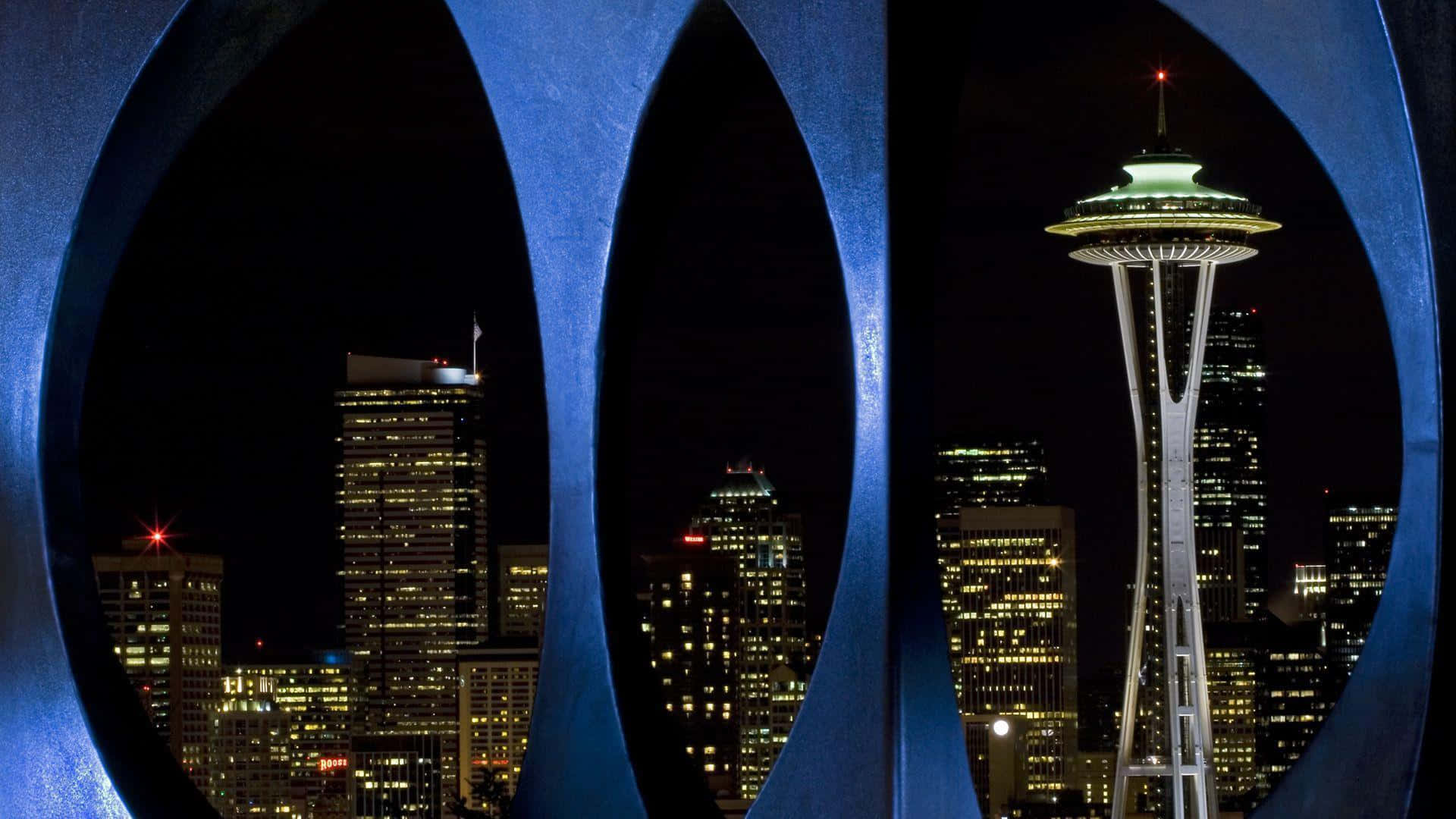 Seattle At Night 桌布 壁紙 — 一個夜晚的西雅圖城市景觀，由大型藍色圓形拱門框住，太空針塔明亮地發光。