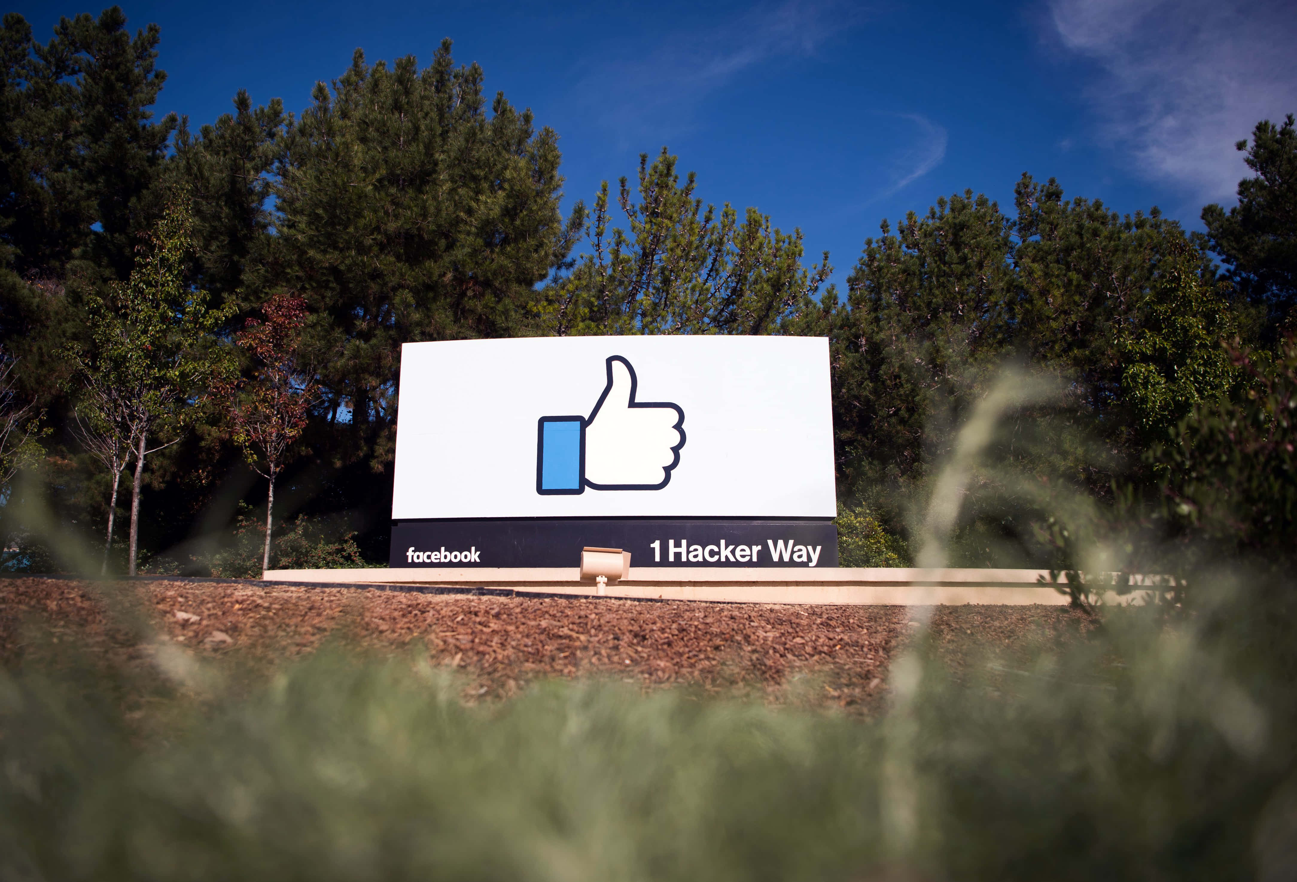 Facebook 桌布 壁紙 — 一個大型Facebook讚好標誌豎立在1 Hacker Way，周圍樹木環繞，天空清澈湛藍。