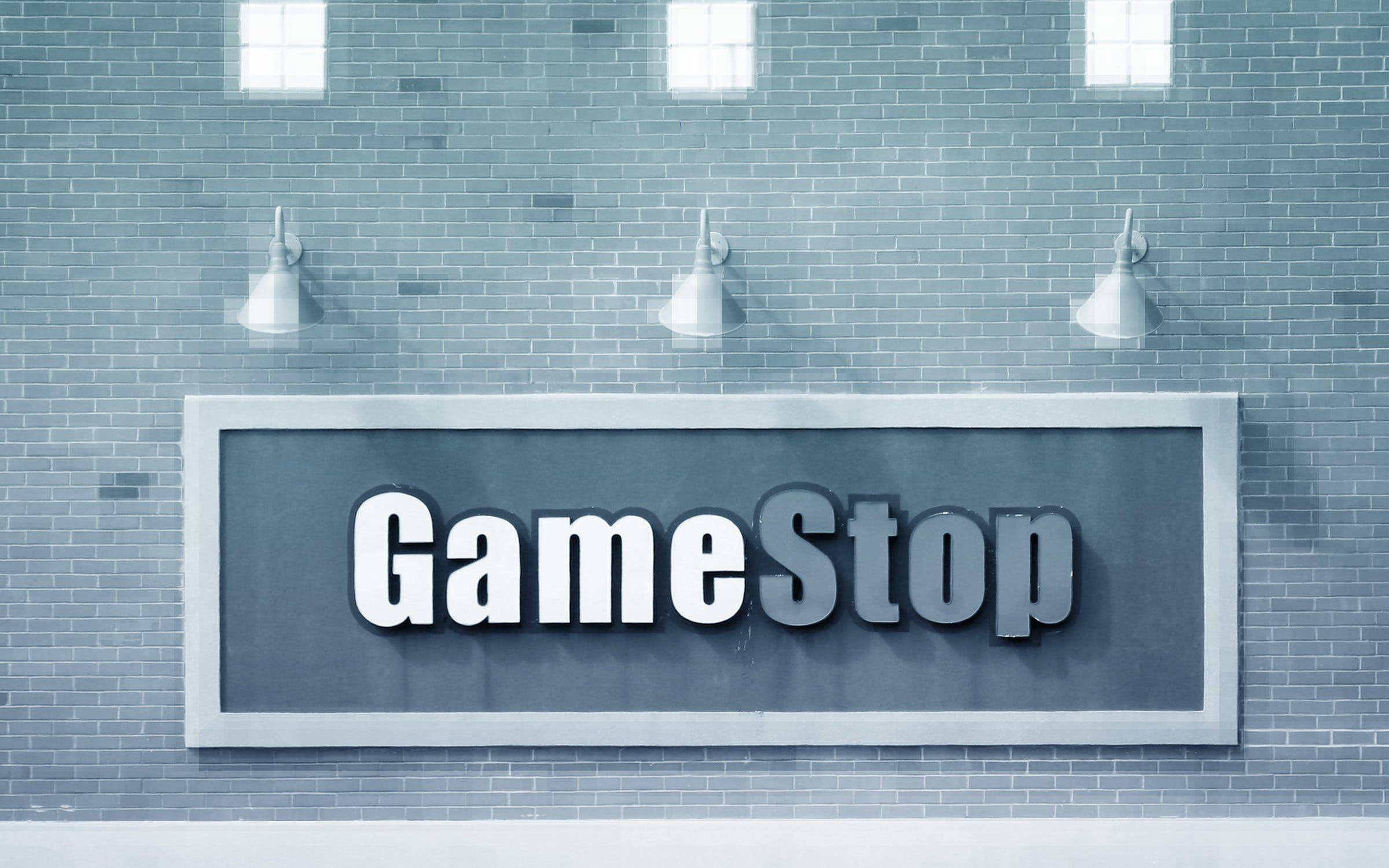 GameStop 桌布 壁紙 — 一個大型GameStop標誌安裝在灰色磚牆上，下方有三盞工業風格的燈。