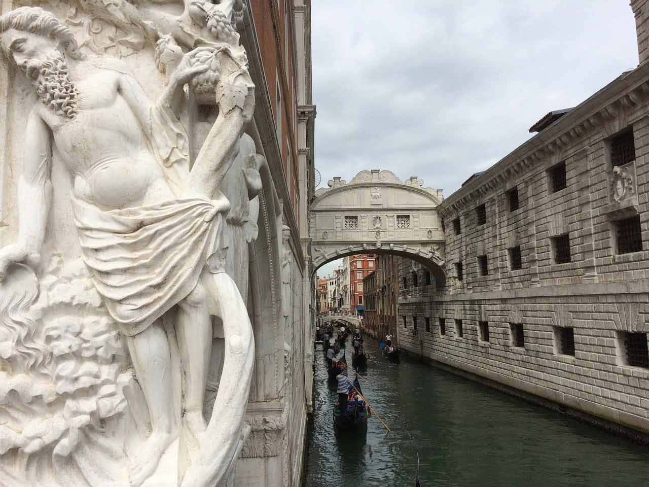 bridge 桌布 壁紙 — 一個大型大理石雕塑框住一條狹窄的威尼斯運河，在陰天時有貢多拉穿過標誌性的嘆息橋下。