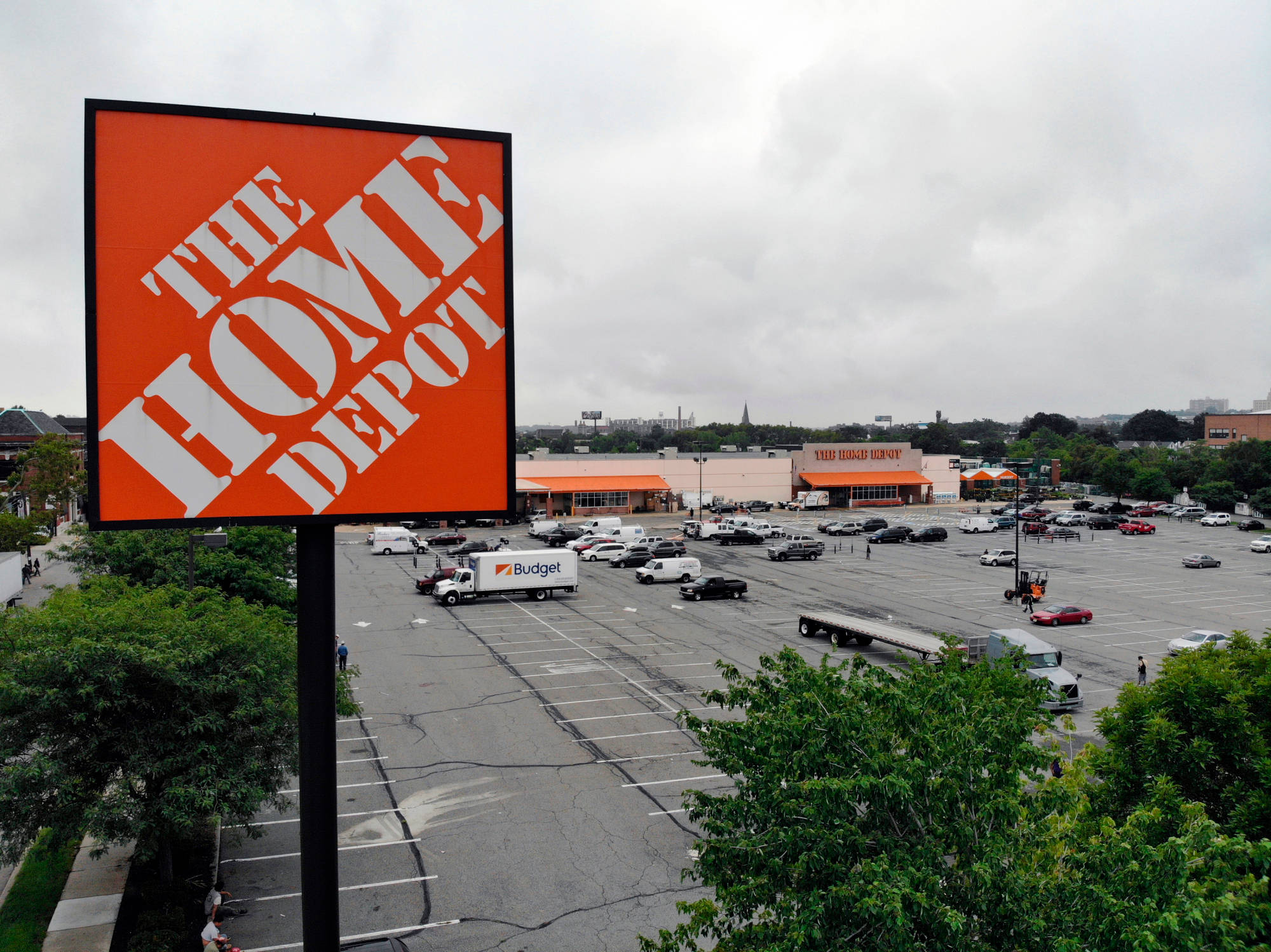 Home Depot 桌布 壁紙 — 一個大型橙色Home Depot標誌在繁忙的停車場上，停滿了汽車和卡車，主導著多雲的一天。