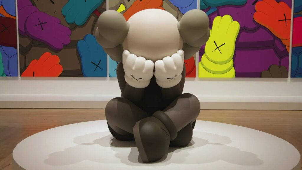 kaws pc 桌布 壁紙 — 一個大型灰色KAWS雕塑盤腿坐在白色底座上，雙手遮眼，背景是色彩繽紛的壁畫。