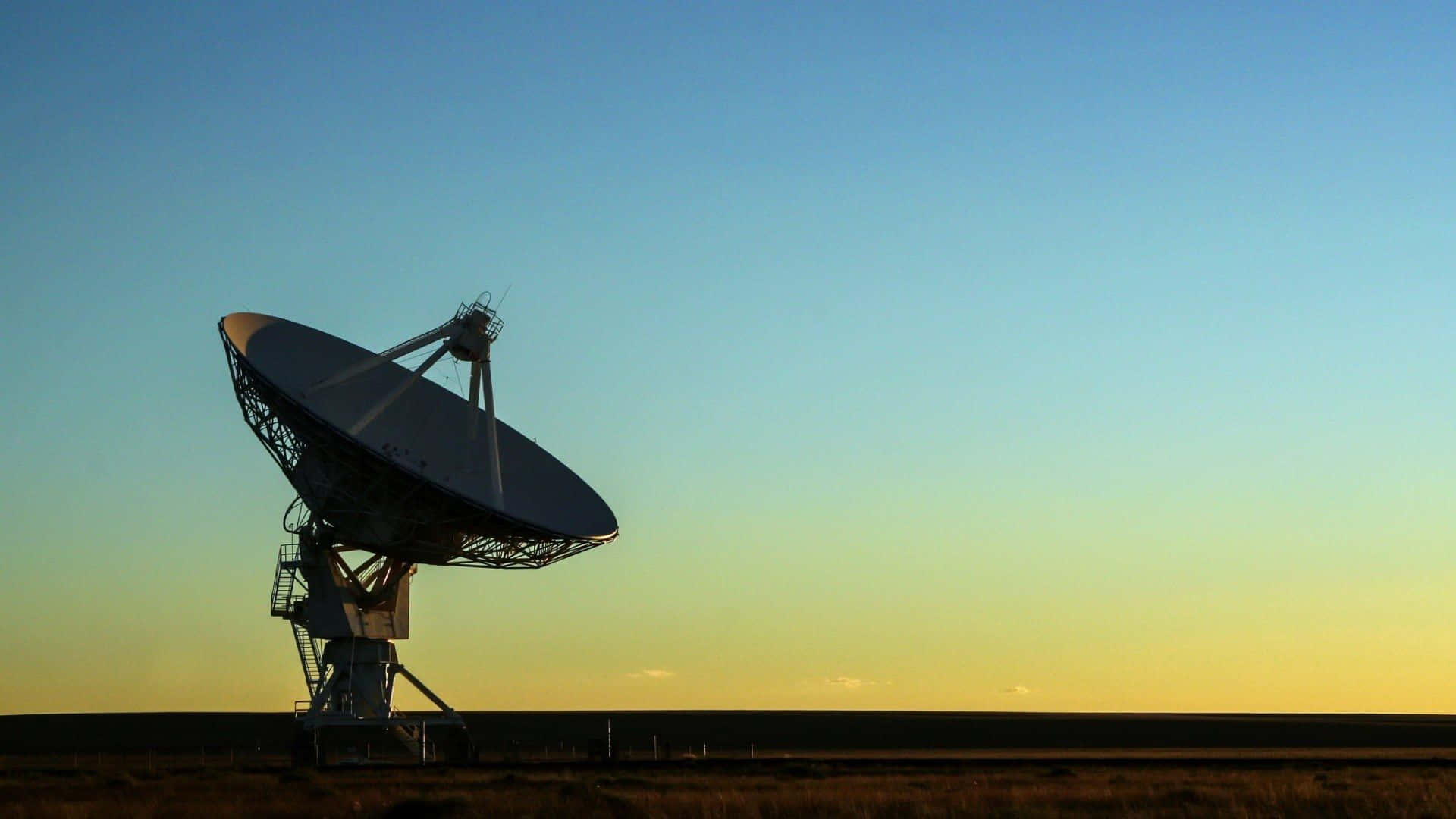 Radio Telescope 桌布 壁紙 — 一個大型無線電望遠鏡在日落時分，以漸變天空為背景，在平坦的沙漠景觀上呈現剪影。