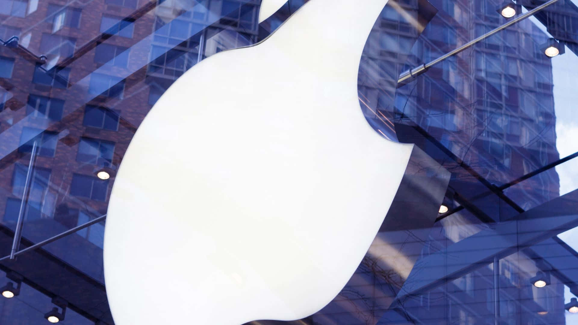 蘋果標誌 桌布 壁紙 — 一個大型白色Apple標誌在藍色玻璃摩天大樓和聚光燈的背景下閃耀。