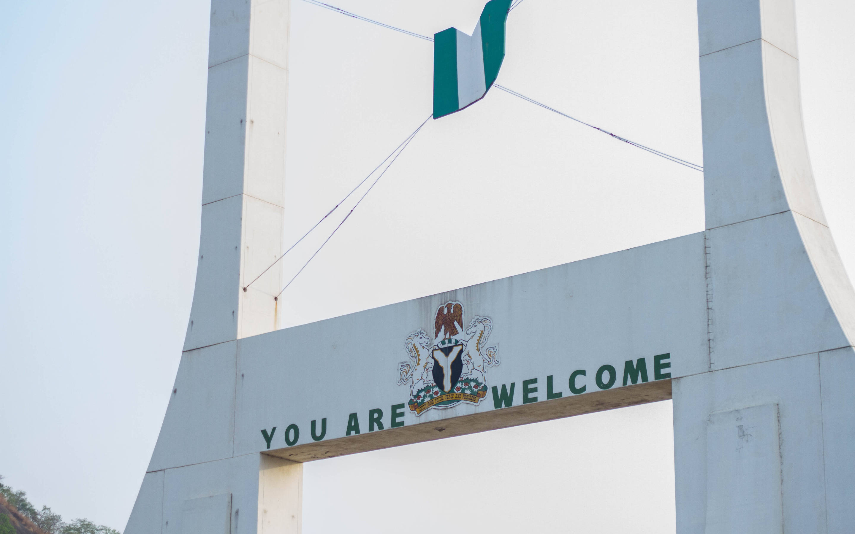 Nigeria 桌布 壁紙 — 一個大型白色拱門，上面寫著「YOU ARE WELCOME」和奈及利亞的國徽，下方飄揚著綠白綠旗。