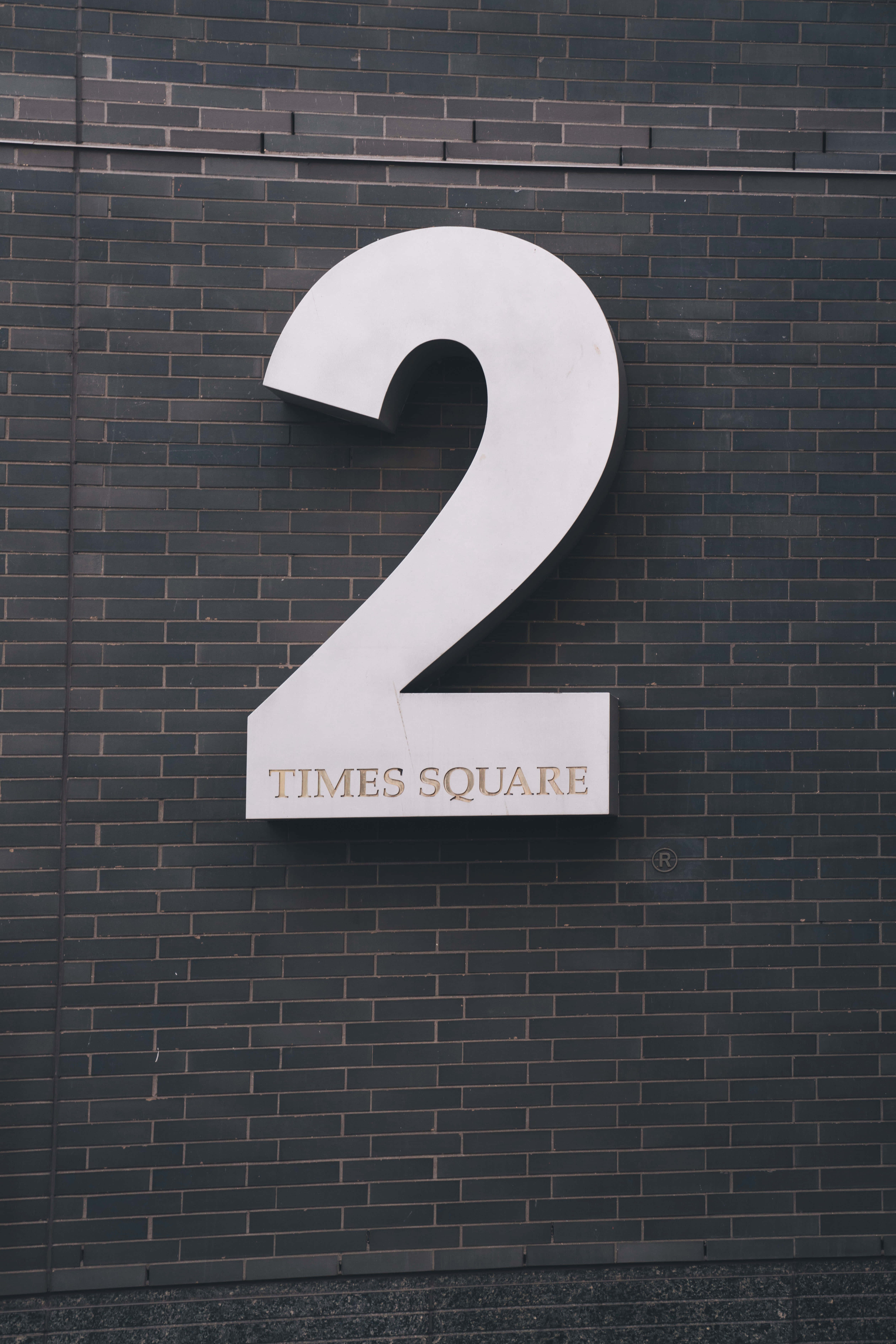Number 2 桌布 壁紙 — 一個大型白色數字二標誌，上面有'TIMES SQUARE'文字，安裝在深灰色磚牆上。