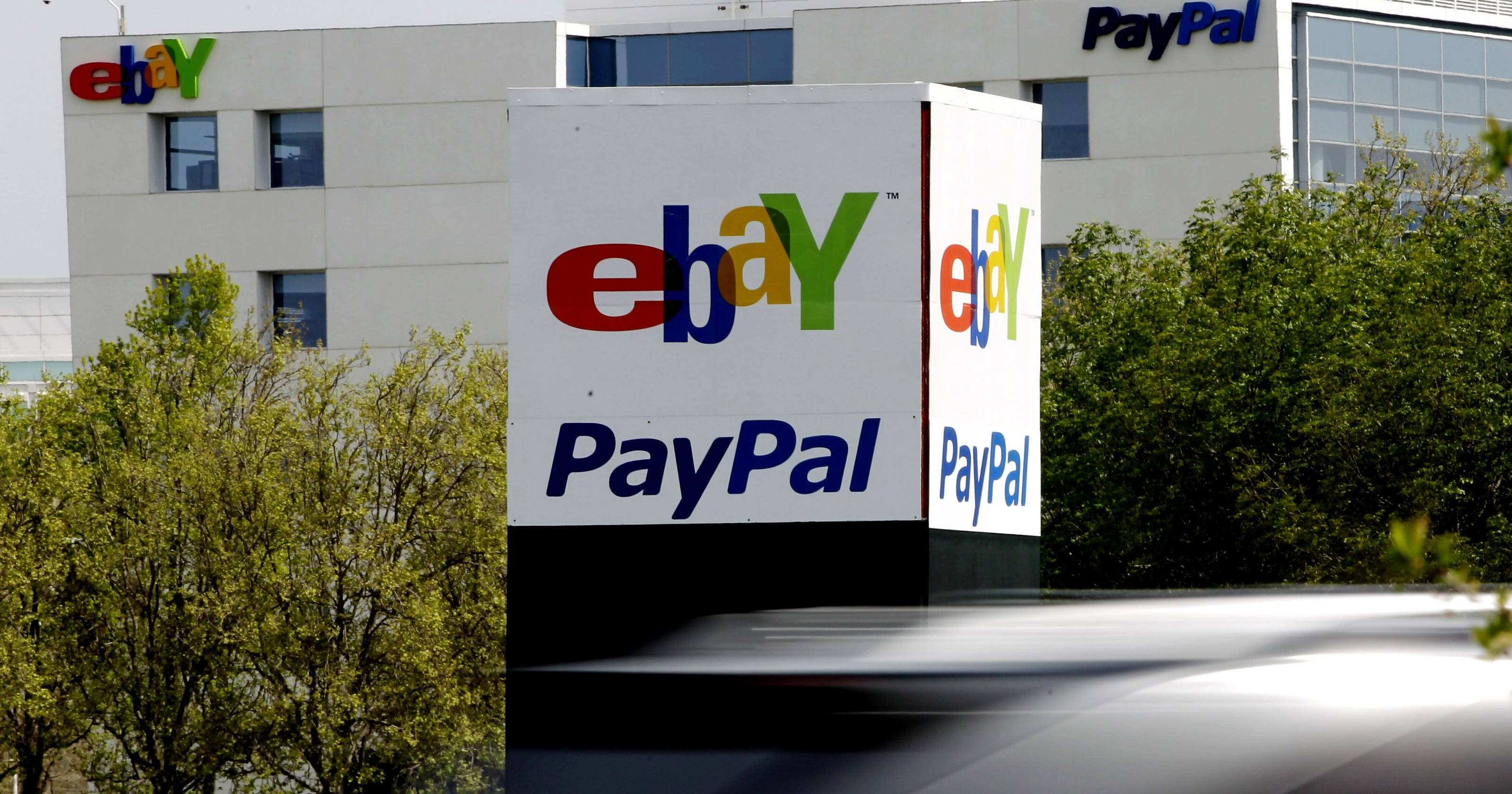 eBay 桌布 壁紙 — 一個大型白色標牌展示色彩繽紛的eBay和藍色PayPal標誌，矗立在一棟現代辦公樓前，前景有綠色樹木。