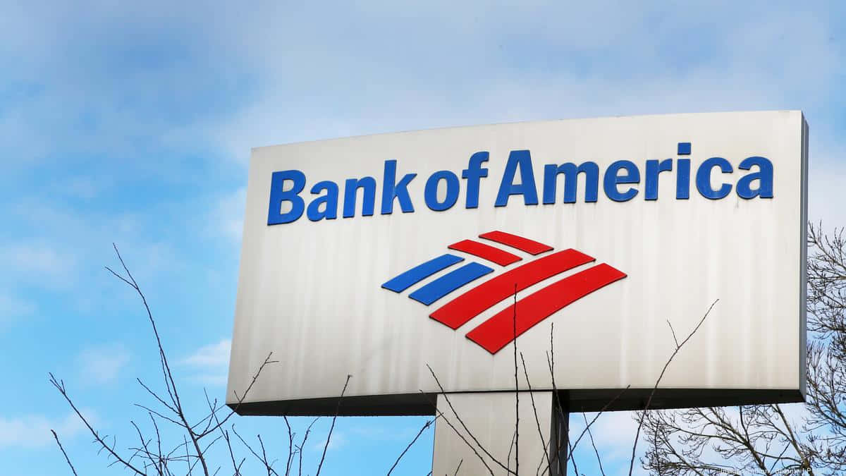 Bank Of America 桌布 壁紙 — 一個大型白色美國銀行標誌，帶有藍紅色的標誌，在明亮的藍天下，前景有光禿的樹枝。