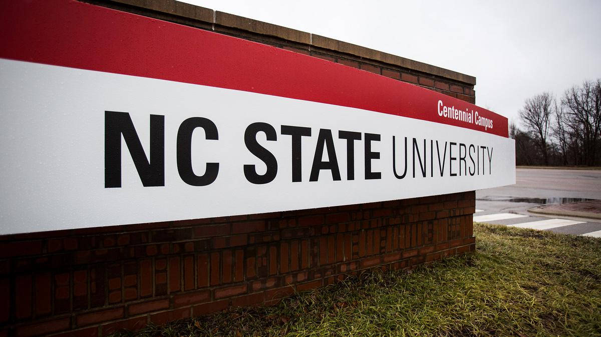 學校 桌布 壁紙 — 一個大型磚製標誌，標示NC State University Centennial Campus，矗立在潮濕的草地上，天空多雲。
