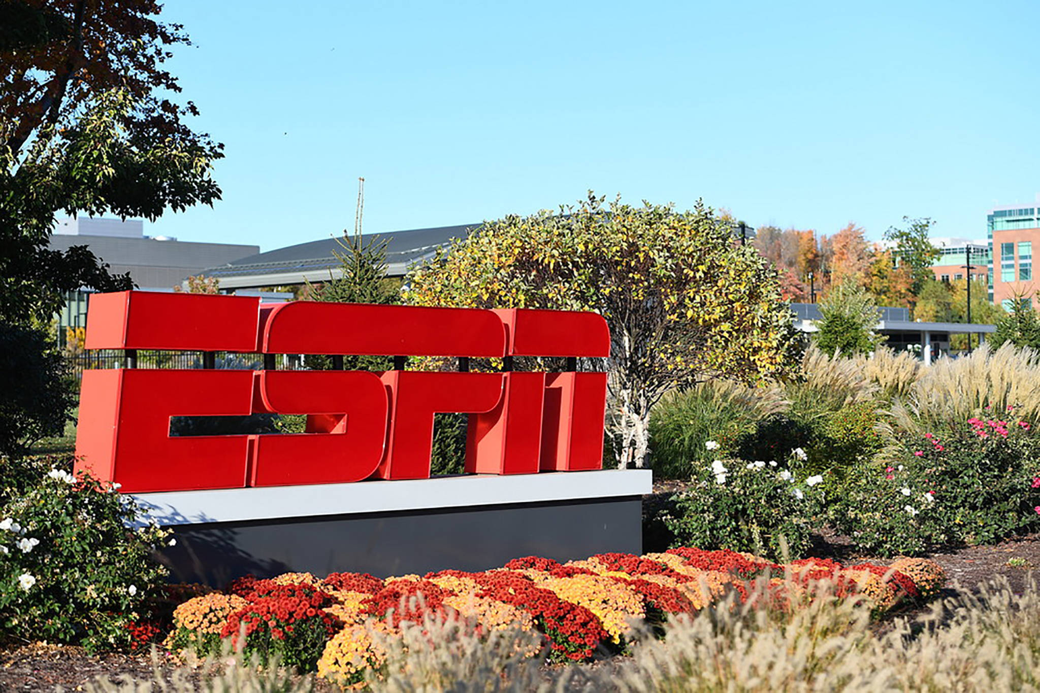 ESPN 桌布 壁紙 — 一個大型紅色ESPN標誌在晴朗藍天下，矗立於種有秋花和樹木的園林花園中，格外顯眼。