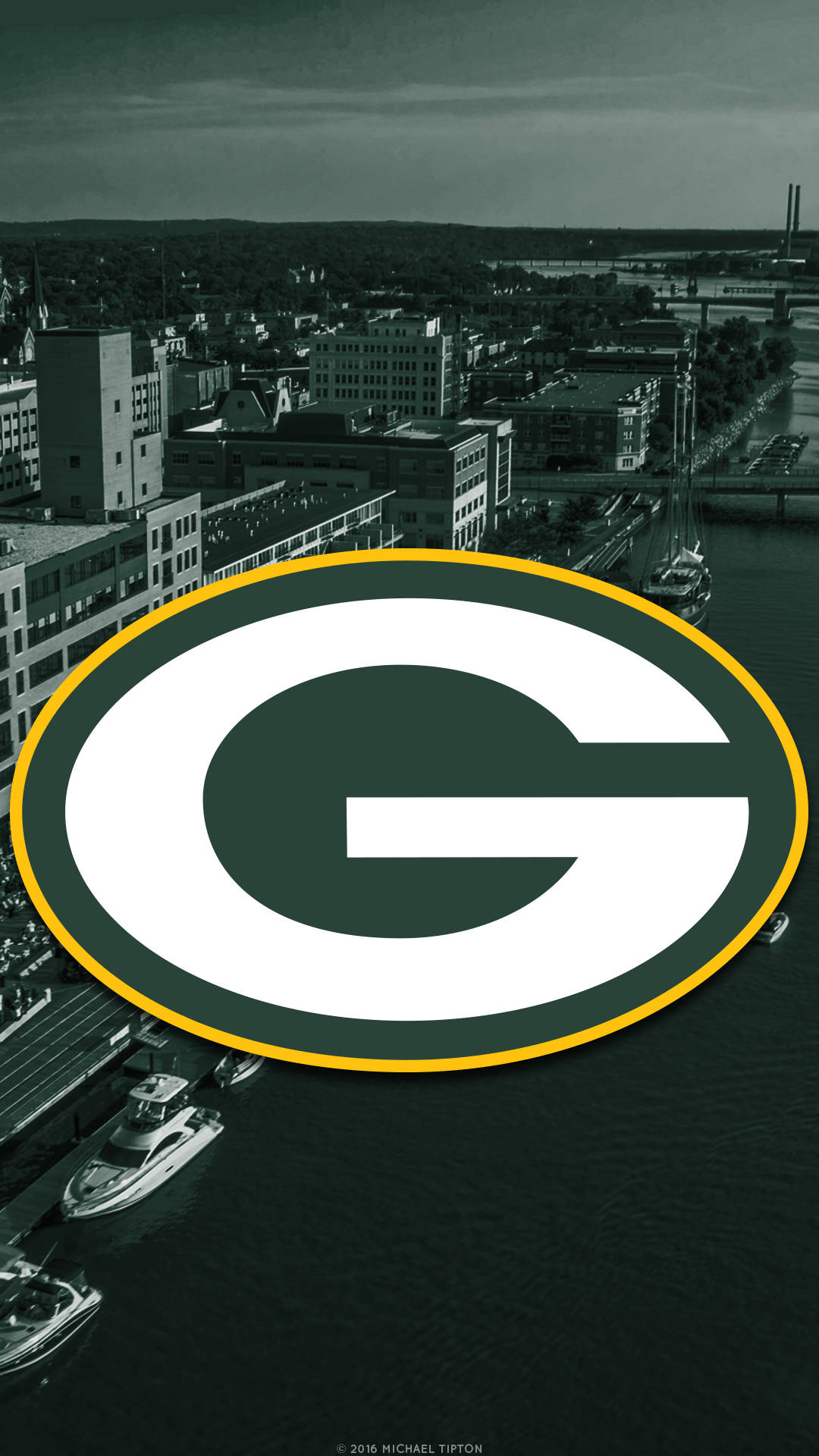 Packers 桌布 壁紙 — 一個大型綠灣包裝工標誌主導了單色城市海濱場景，有船隻和建築物。