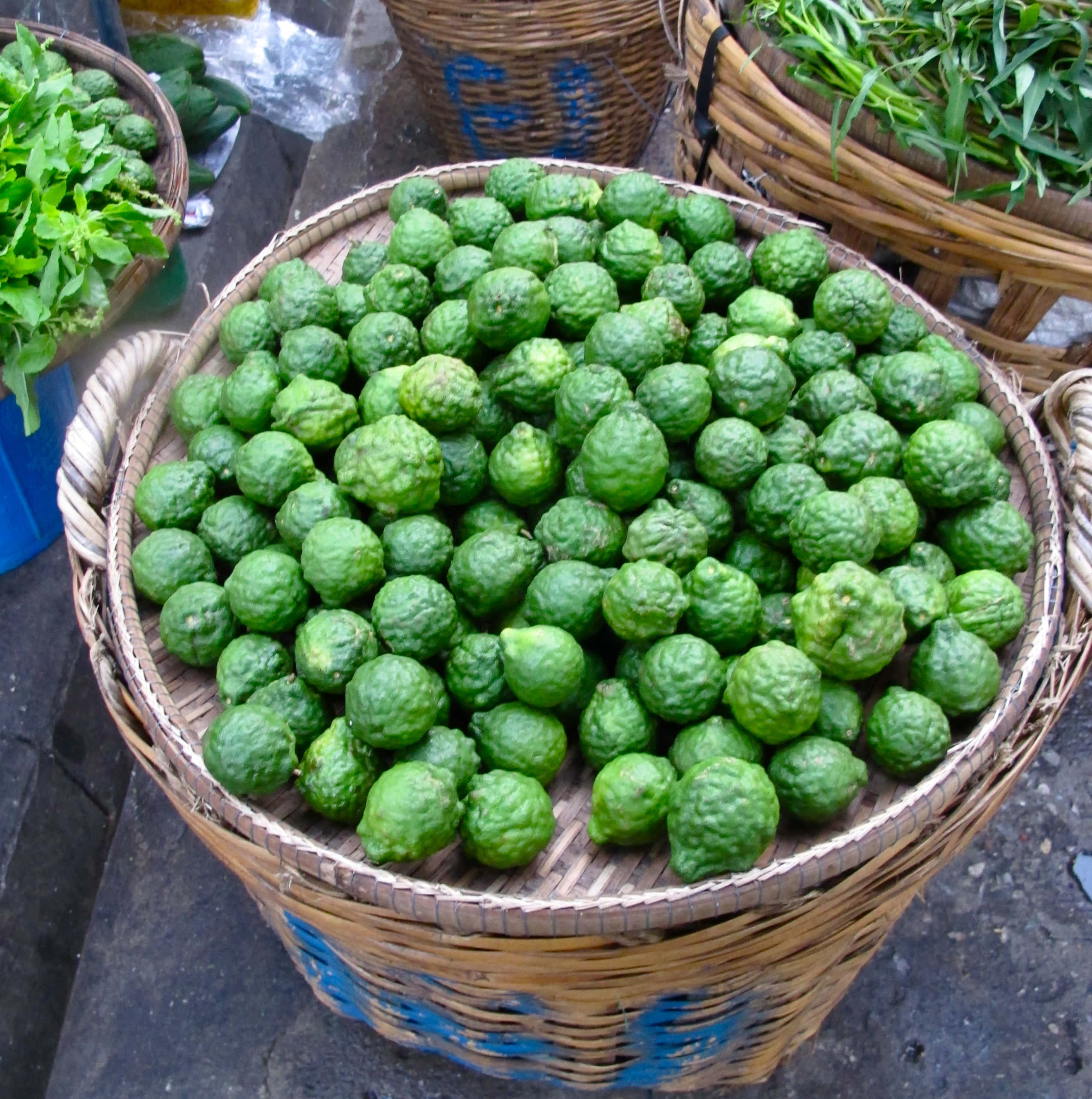 Fruit 桌布 壁紙 — 一個大型編織籃，裝滿了鮮綠色、凹凸不平的泰國青檸，在熱鬧的戶外市場攤位上。