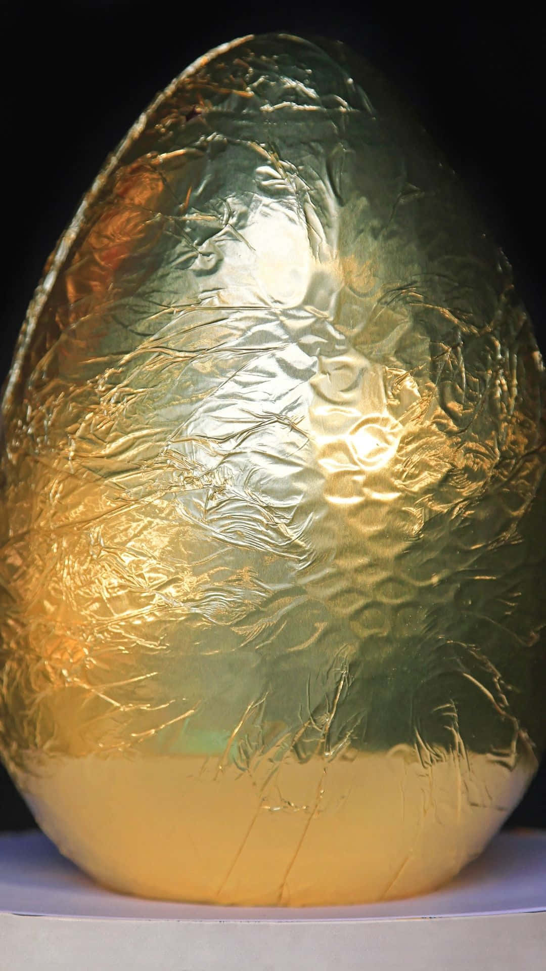 Easter Egg 桌布 壁紙 — 一個大型華麗的金色箔紙包裹的蛋，帶有皺紋質感和溫暖的高光，背景為黑色。