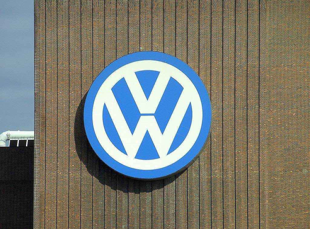 品牌 桌布 壁紙 — 一個大型藍白 Volkswagen 標誌安裝在棕色磚建築上，天空晴朗。