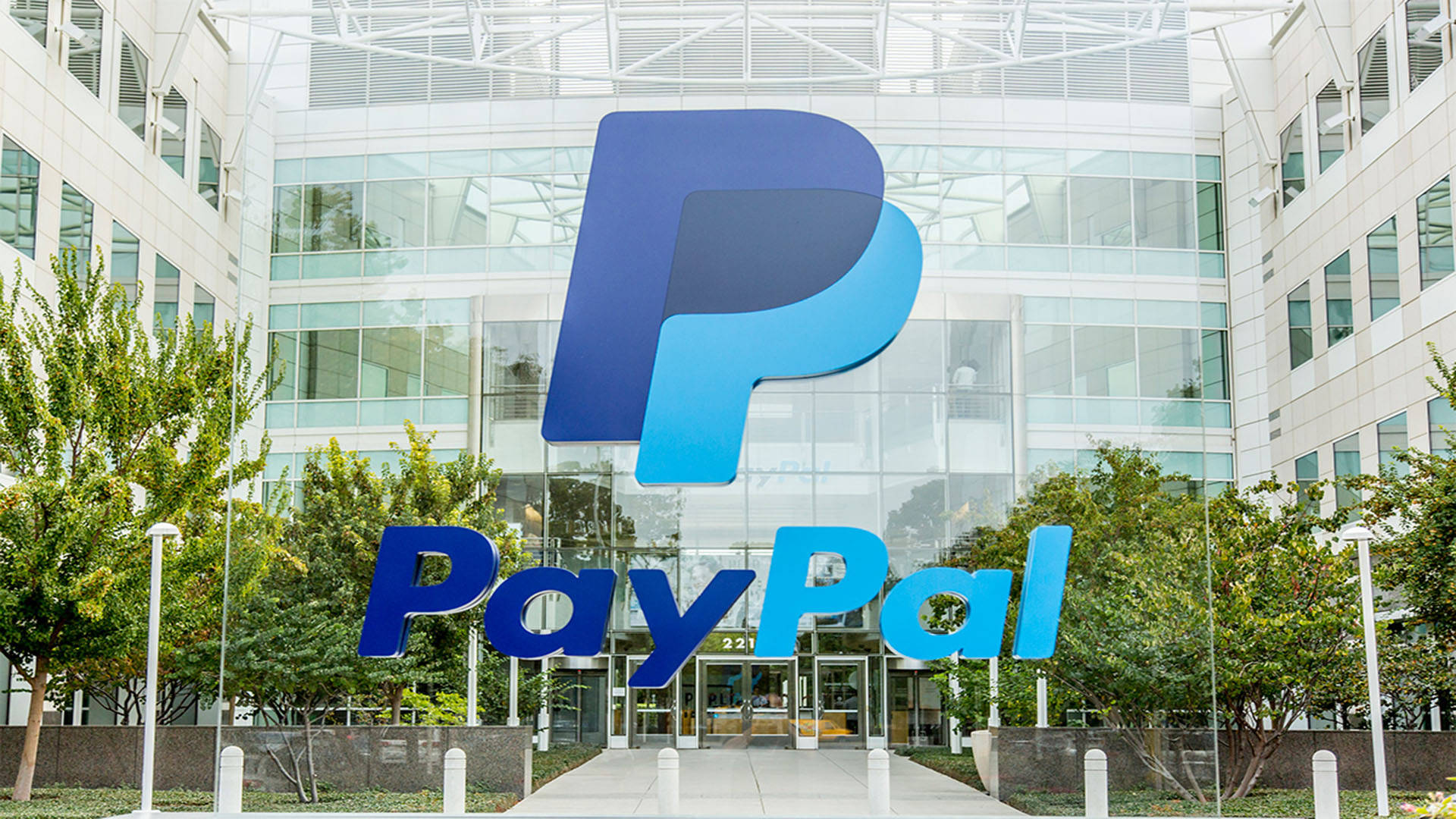 PayPal 桌布 壁紙 — 一個大型藍色PayPal標誌醒目地矗立在一棟被綠樹環繞的現代玻璃建築前。