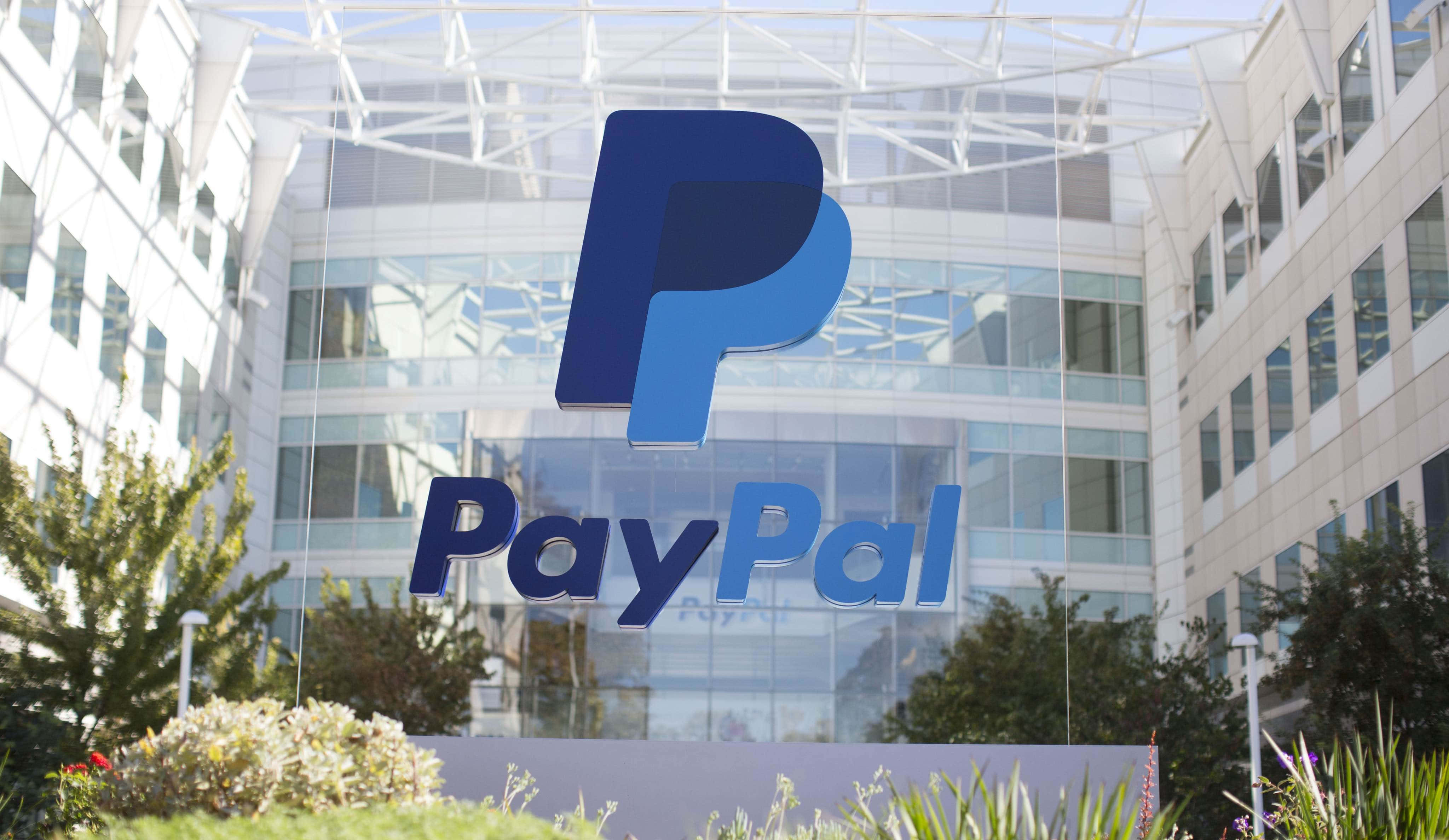 PayPal 桌布 壁紙 — 一個大型藍色PayPal標誌醒目地矗立在一棟現代辦公大樓的玻璃外牆上，周圍環繞著綠植。