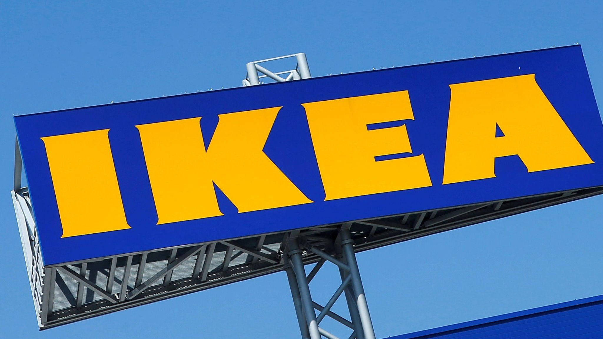 Sweden 桌布 壁紙 — 一個大型藍色和黃色的IKEA標誌，在清晰藍天下，金屬支撐結構清晰可見。
