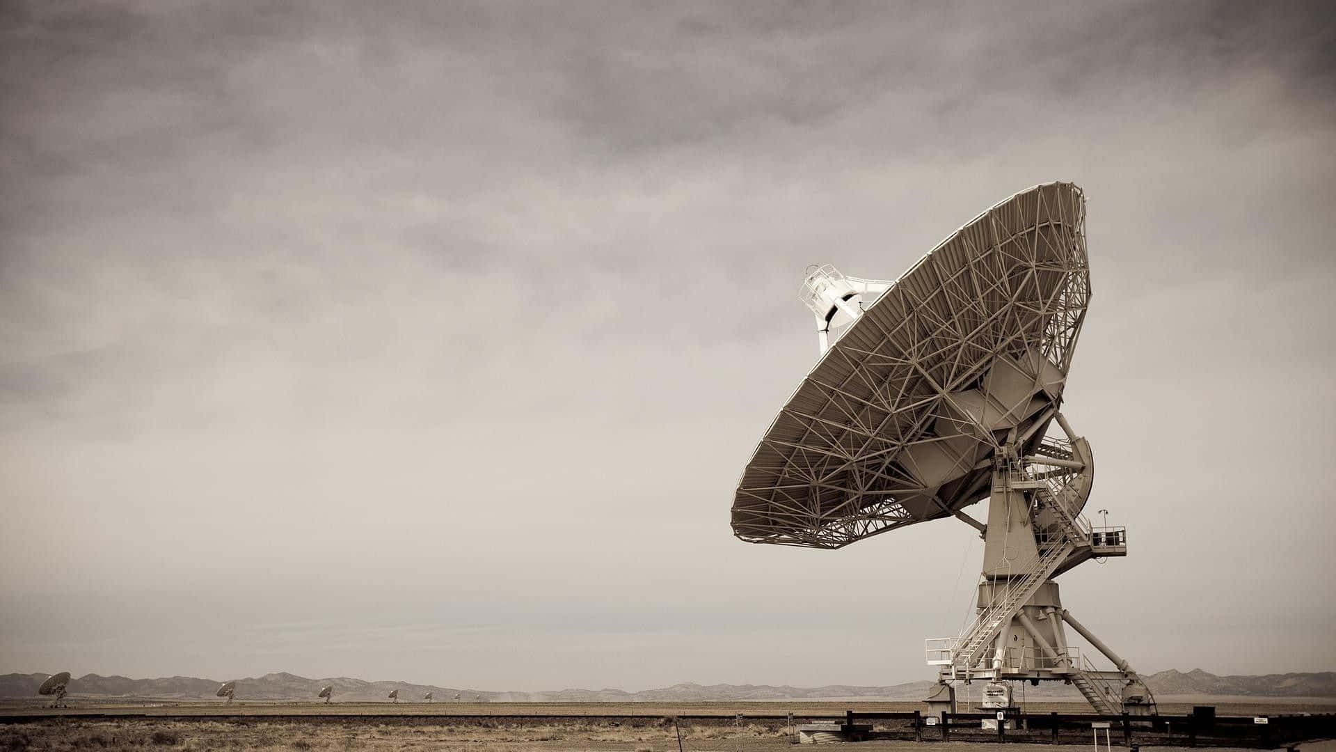 Radio Telescope 桌布 壁紙 — 一個大型衛星天線獨自矗立在廣闊的沙漠中，天空多雲，遠山可見。