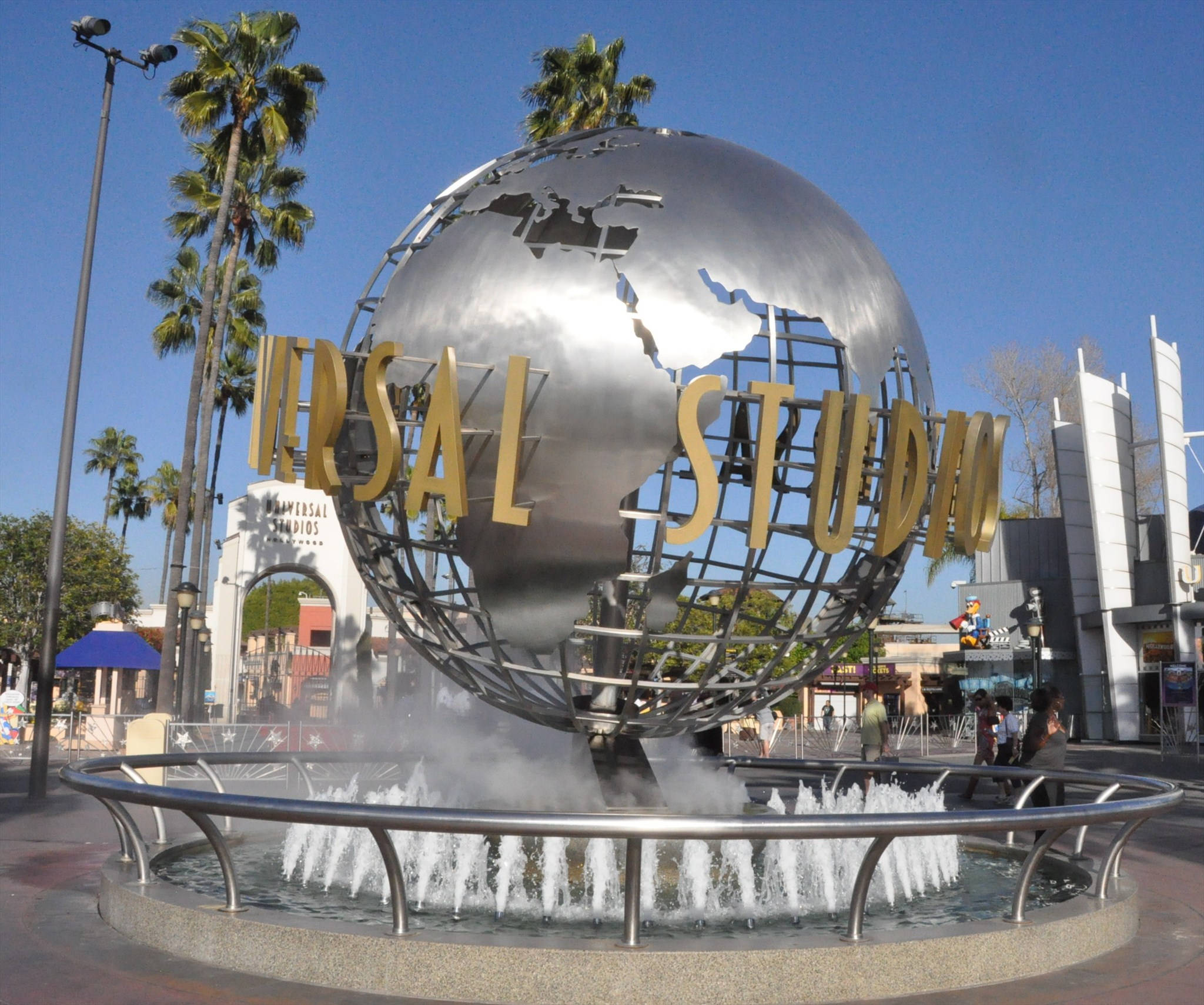 Universal 桌布 壁紙 — 一個大型金屬地球儀，上面有金色的「Universal Studios」字樣，坐落於噴泉頂部，背景有棕櫚樹和清澈的藍天。