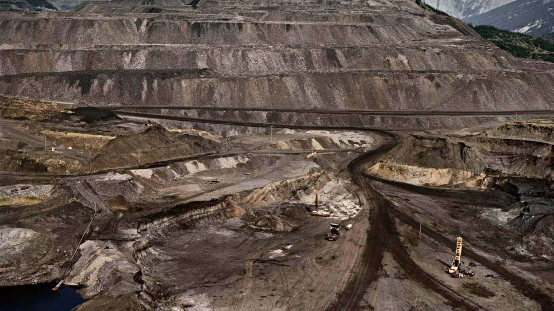 Mining 桌布 壁紙 — 一個大型露天礦場的鳥瞰圖，有梯田狀的岩壁和重型機械在塵土飛揚的道路上作業。