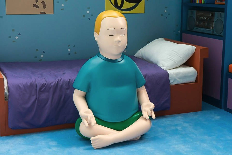 Bobby Hill 桌布 壁紙 — 一個大型風格化的男孩蓮花坐姿雕像，在一個有紫色床單和藍色牆壁的兒童房中平靜地冥想。