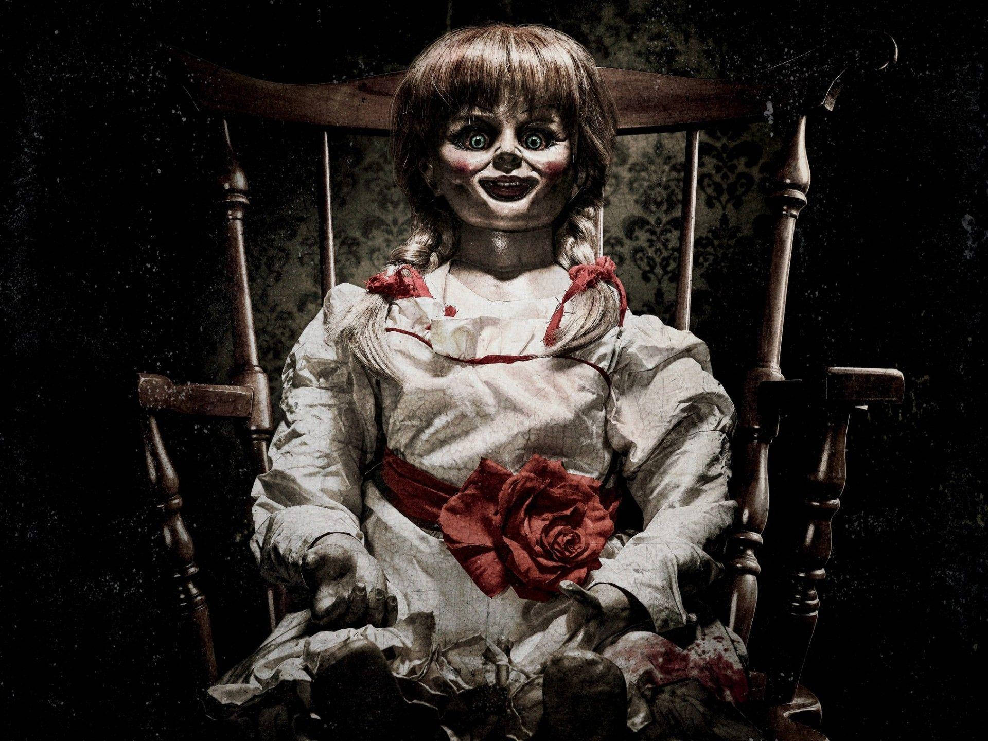 Conjuring 桌布 壁紙 — 一個大眼睛、手持紅玫瑰的恐怖娃娃坐在木搖椅上，背景是深色圖案牆壁。