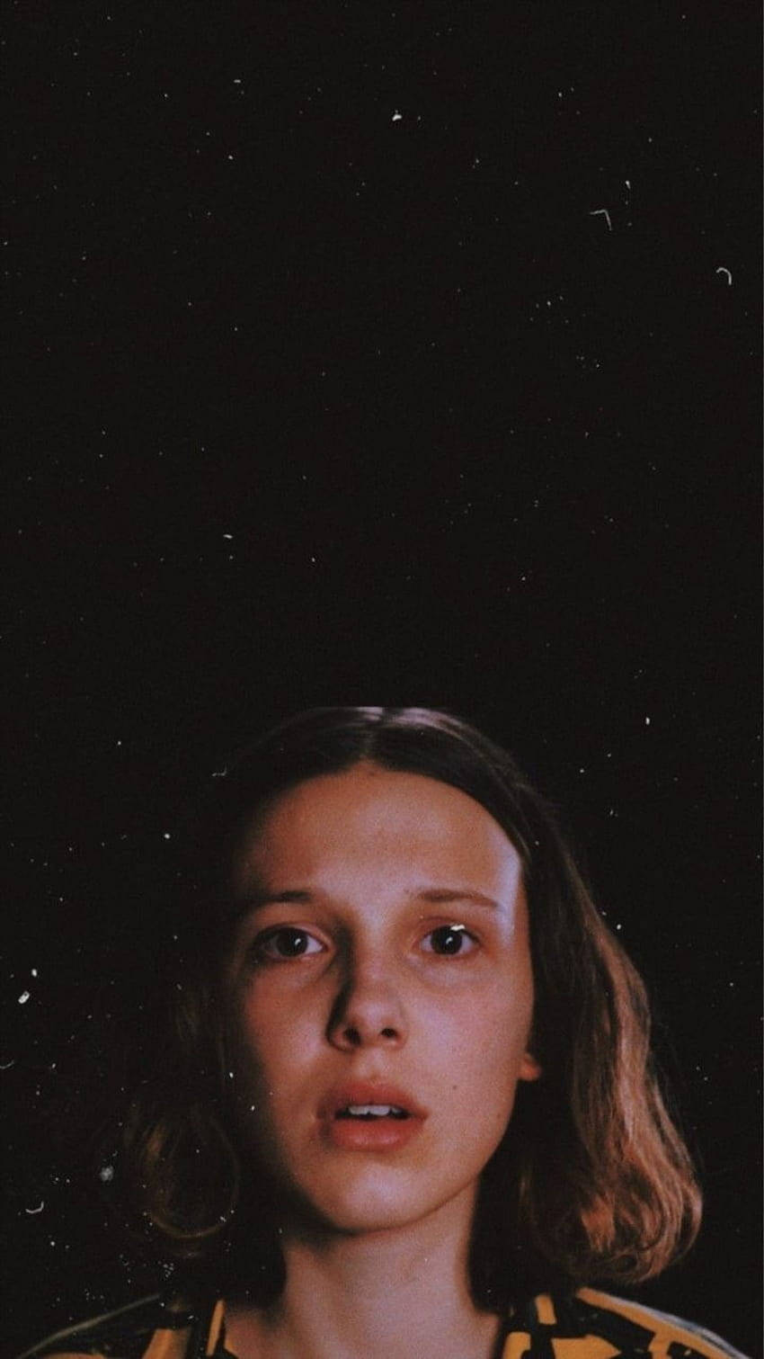 Aesthetic Stranger Things Eleven 桌布 壁紙 — 一個大眼睛的小女孩向上凝視著一個有星星的夜空，帶有輕微的底片顆粒紋理。
